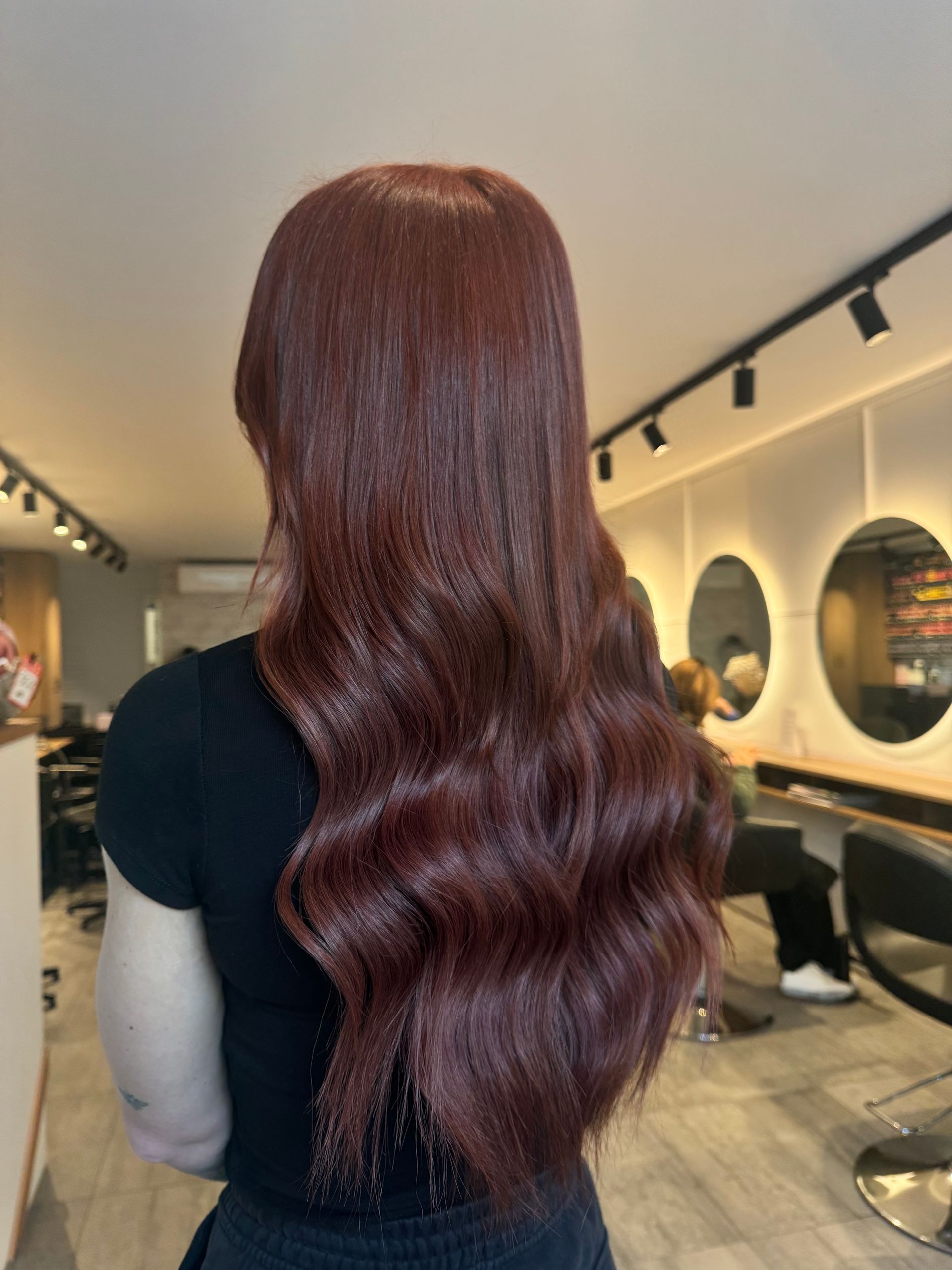A woman with long red hair is standing in a salon.