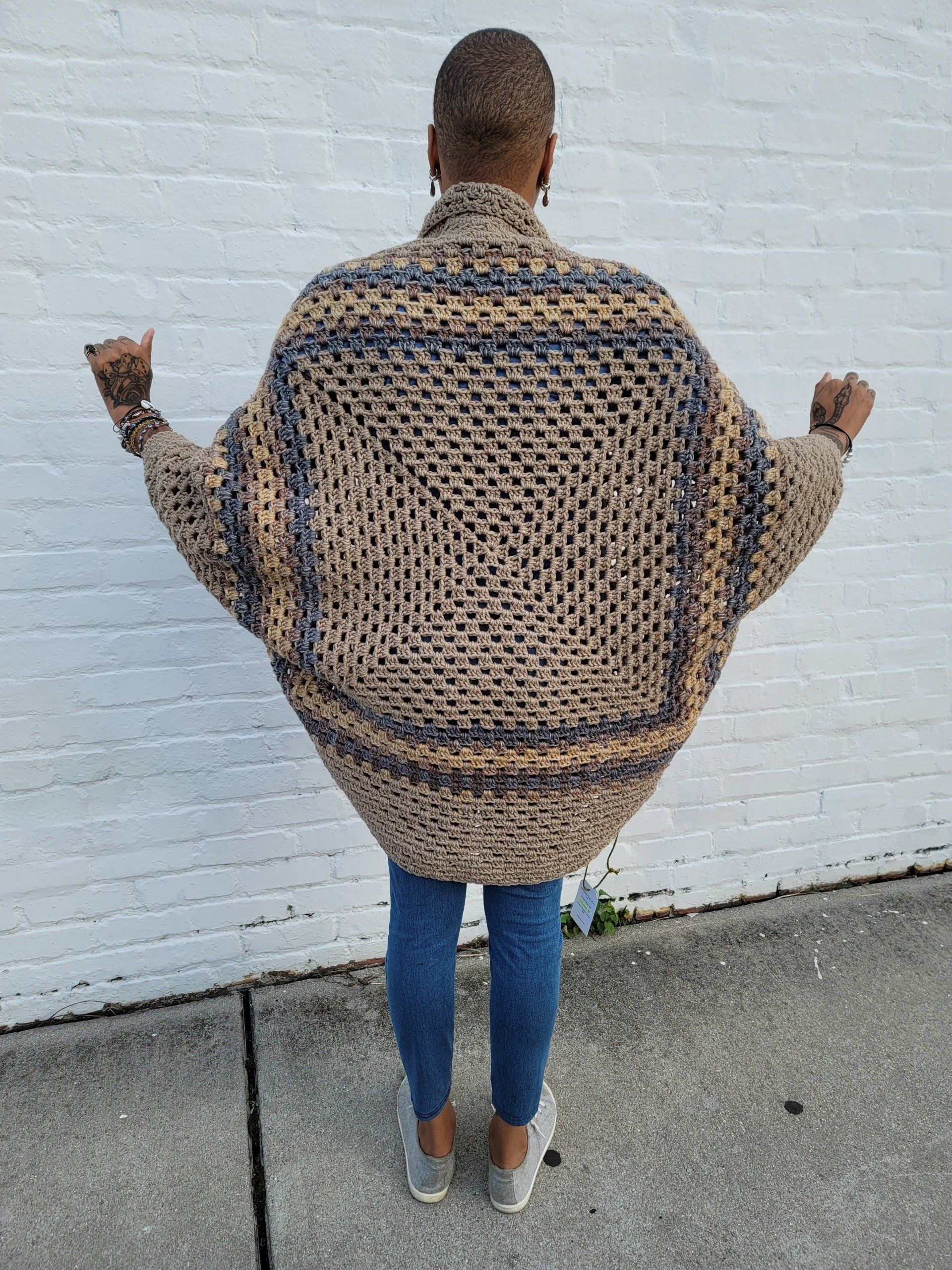 A woman is standing on a sidewalk wearing a crocheted sweater.