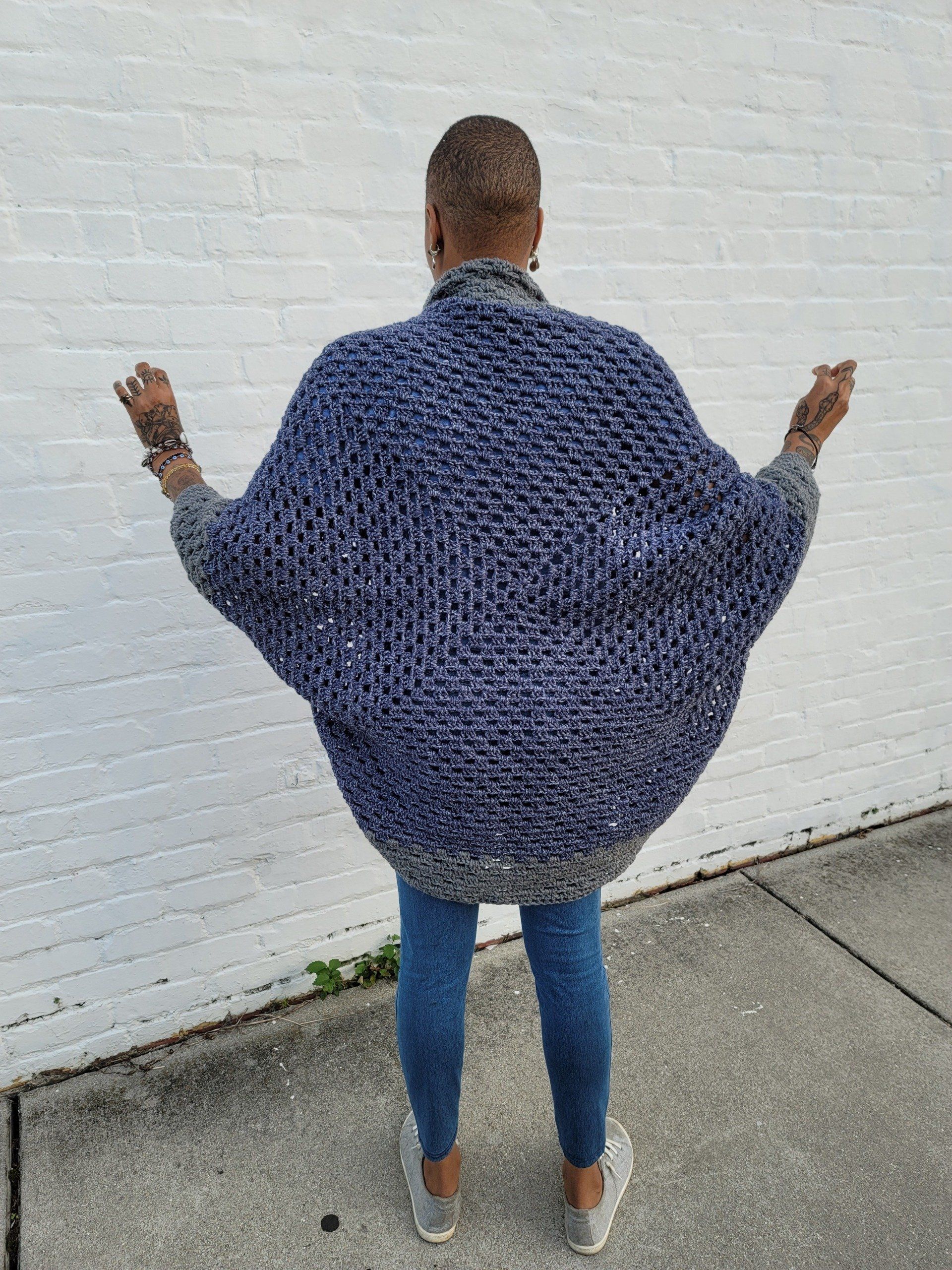 A woman wearing a blue sweater is standing in front of a white brick wall.