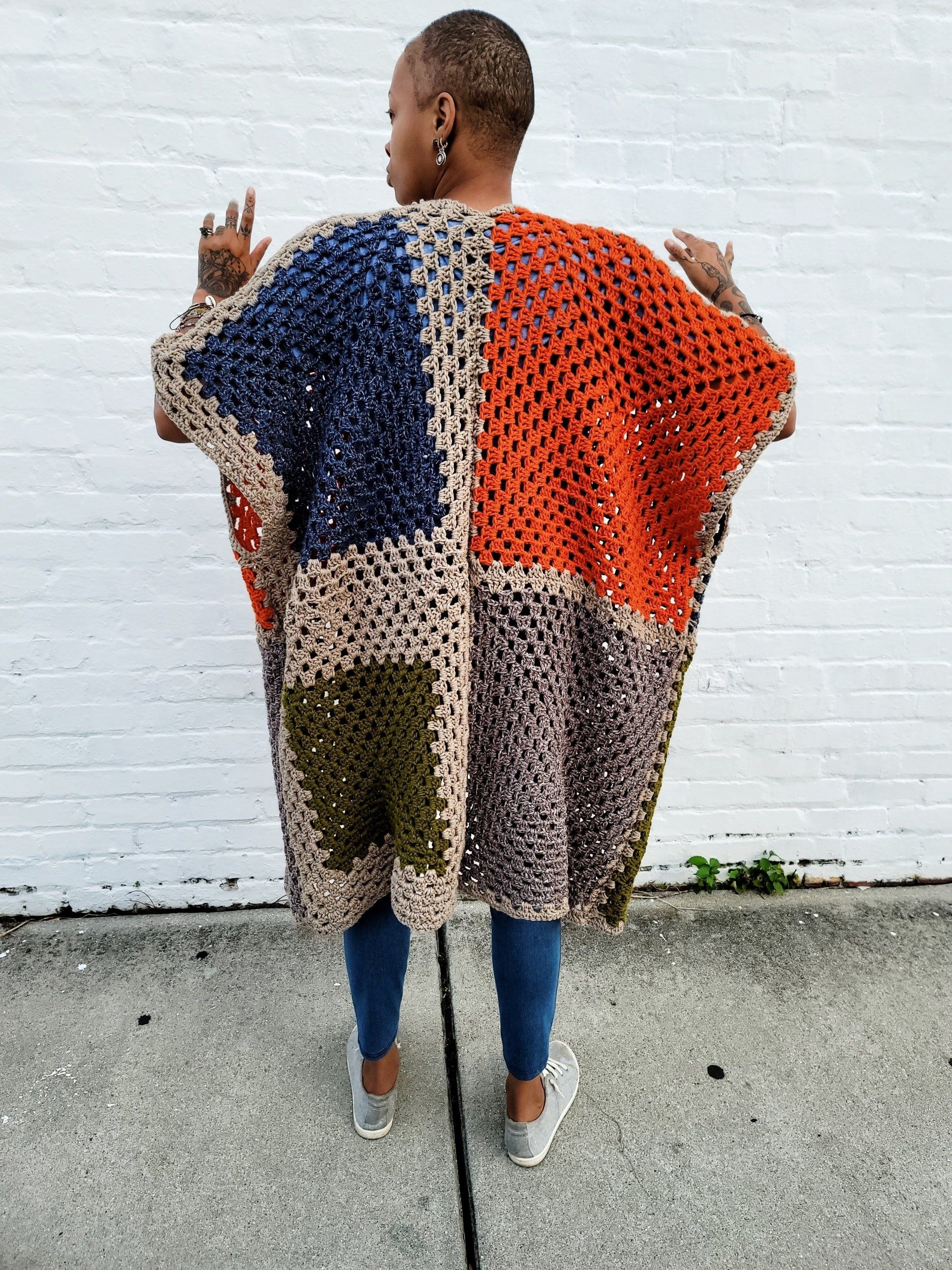 A woman is standing on a sidewalk wearing a crocheted poncho.