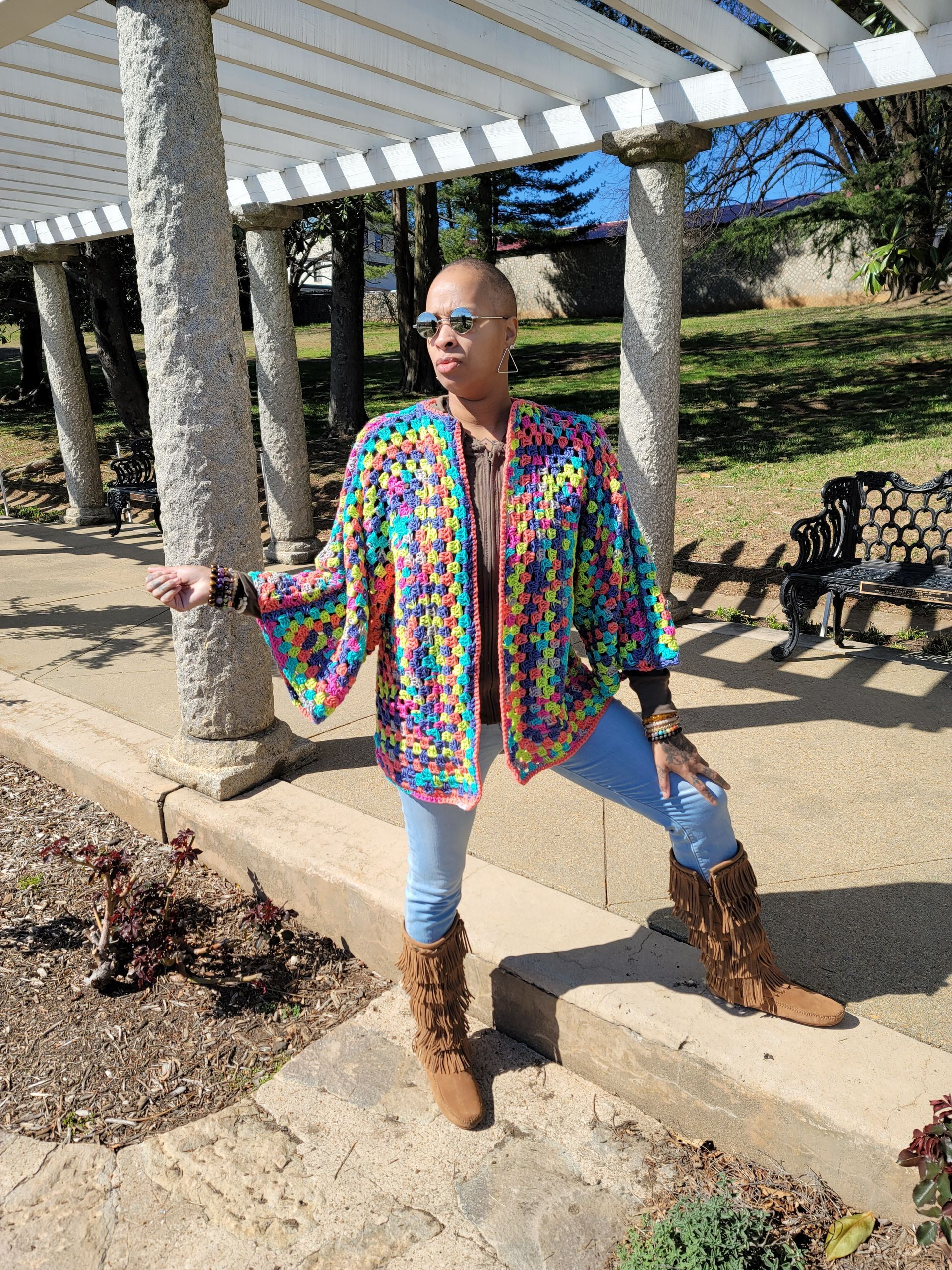 a woman wearing a crocheted cardigan stands with her arms outstretched