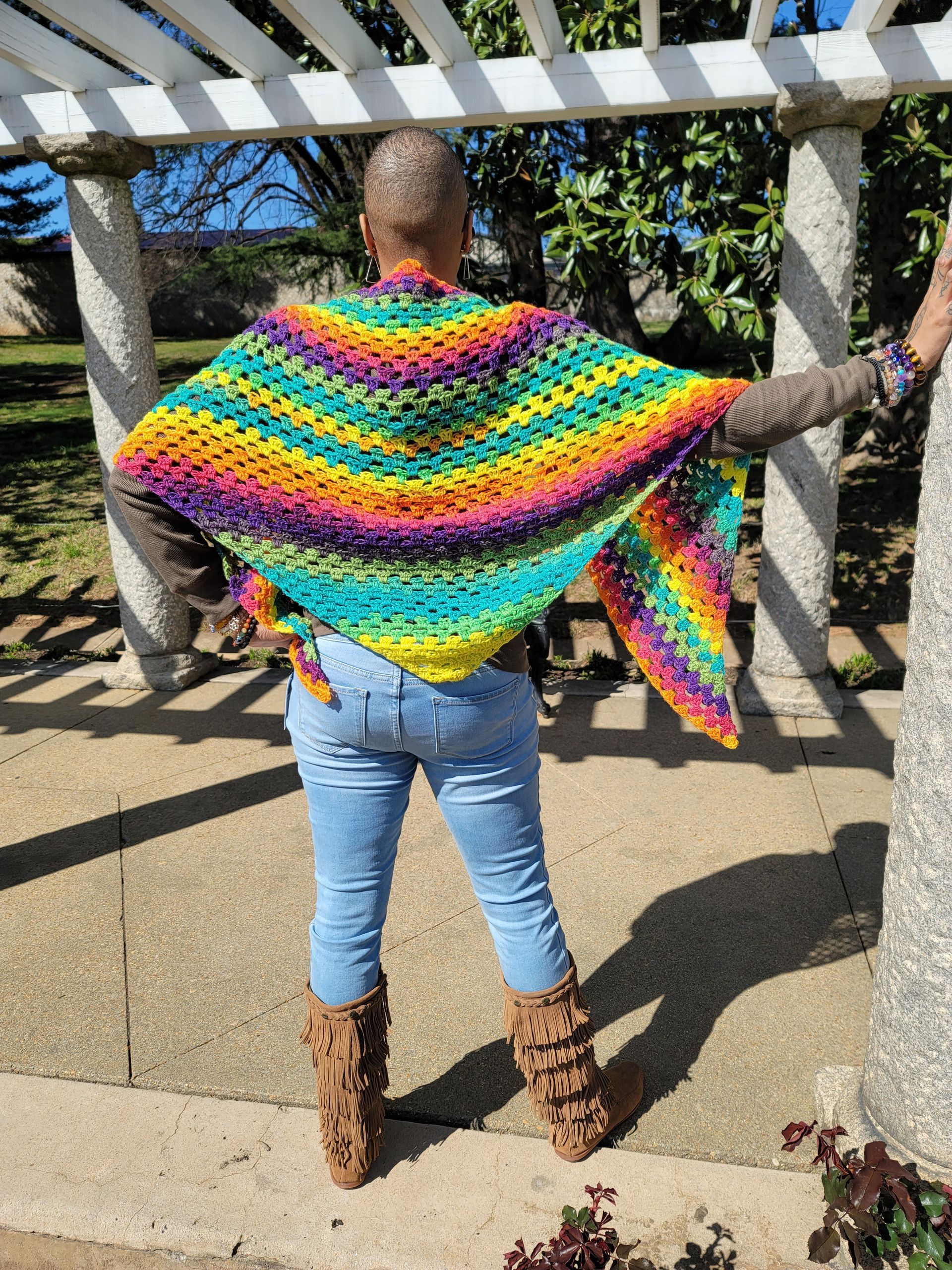A woman is wearing a colorful crocheted shawl over her shoulders.
