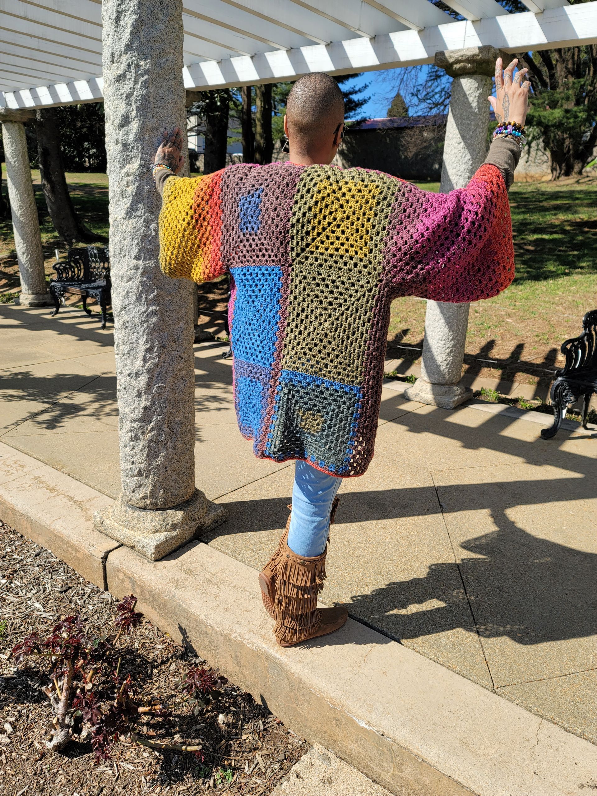 A man is standing on a sidewalk wearing a colorful sweater.
