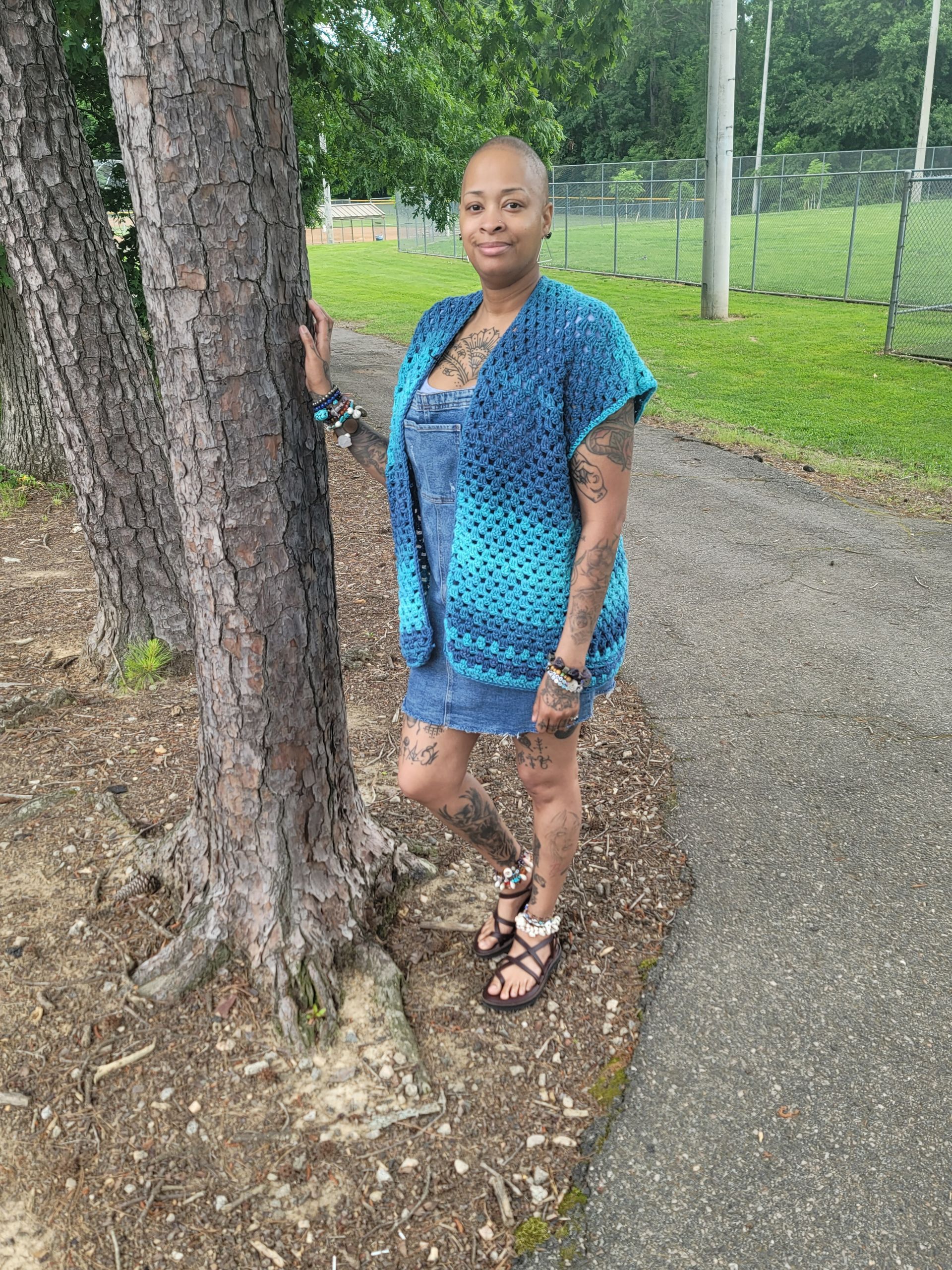A woman in a blue dress is standing next to a tree.
