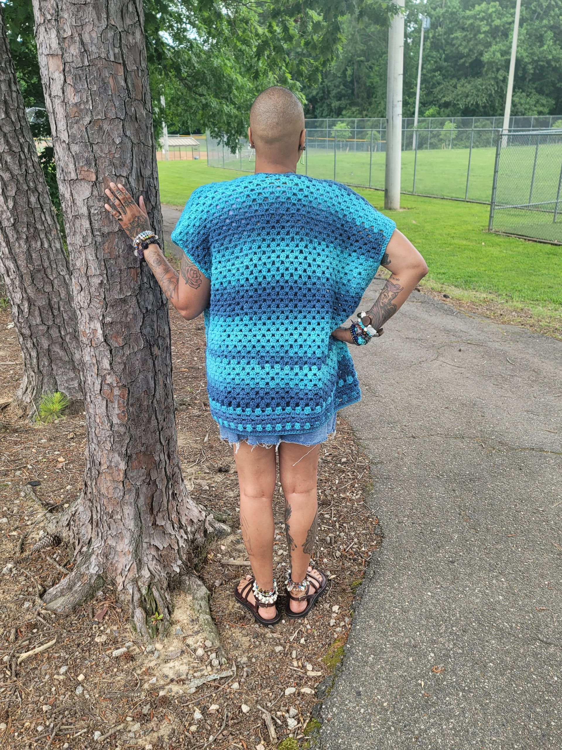 A woman in a blue sweater is standing next to a tree.