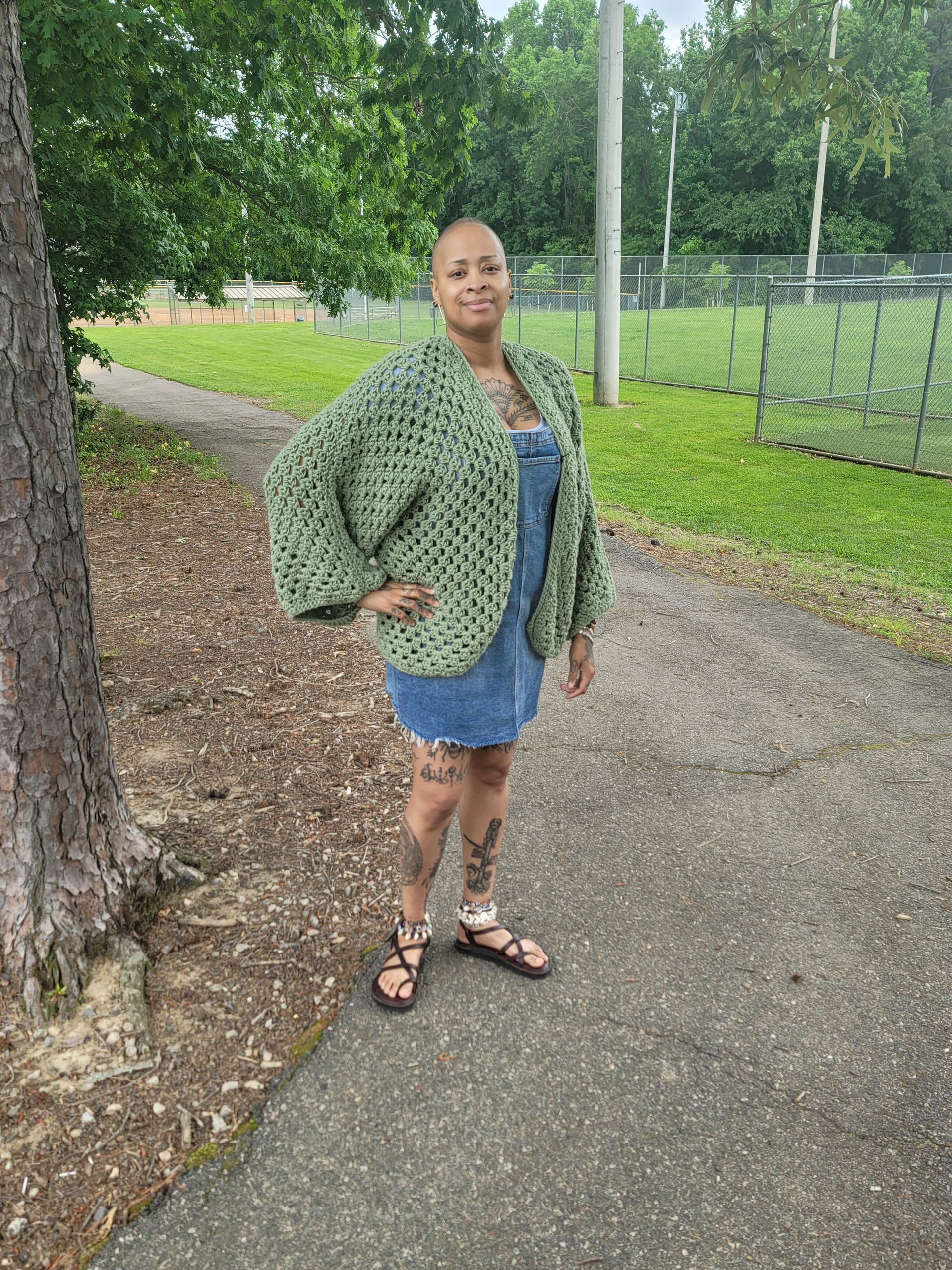A woman is standing on a sidewalk next to a tree.