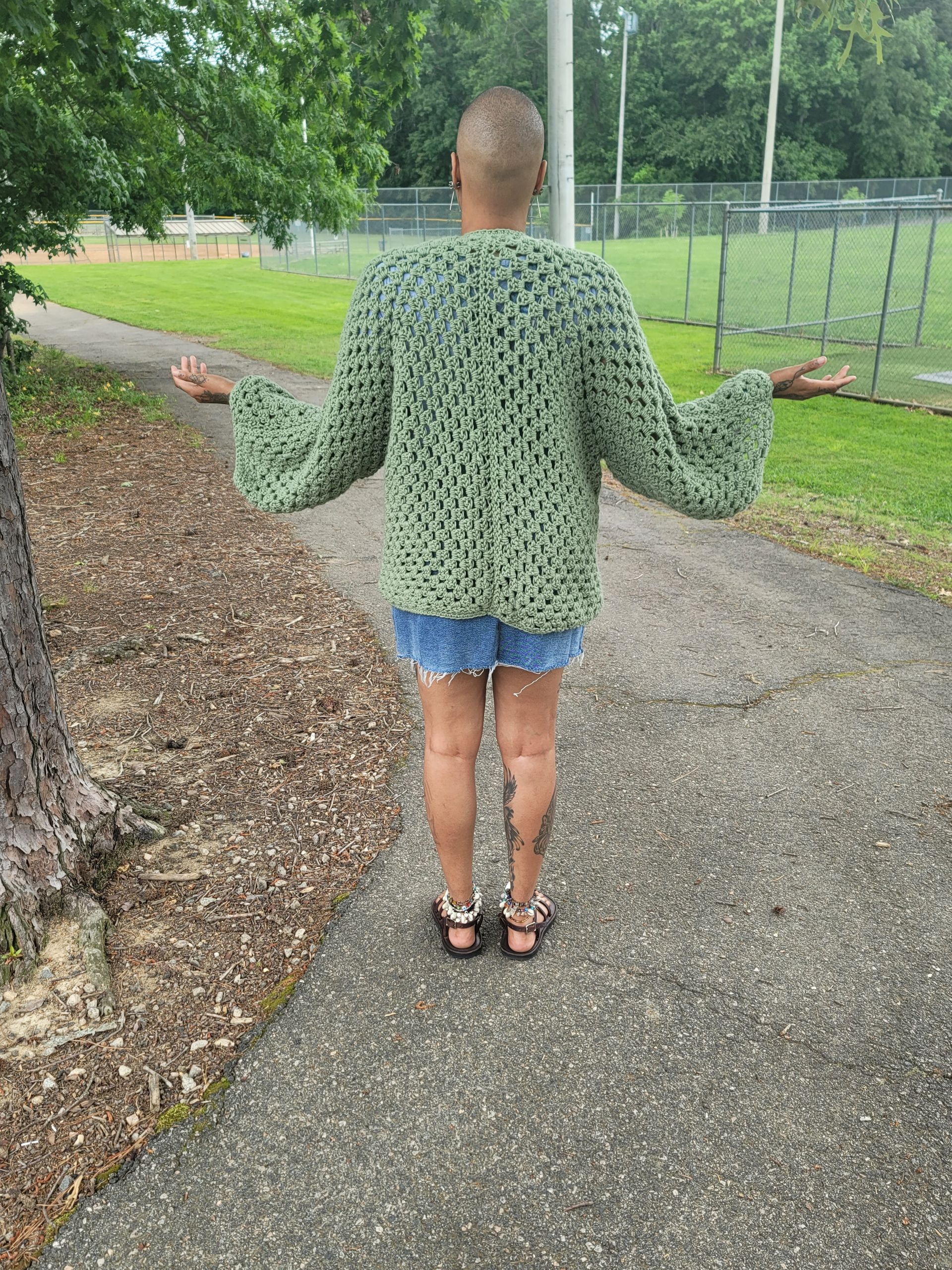 A woman is standing on a sidewalk wearing a green sweater.