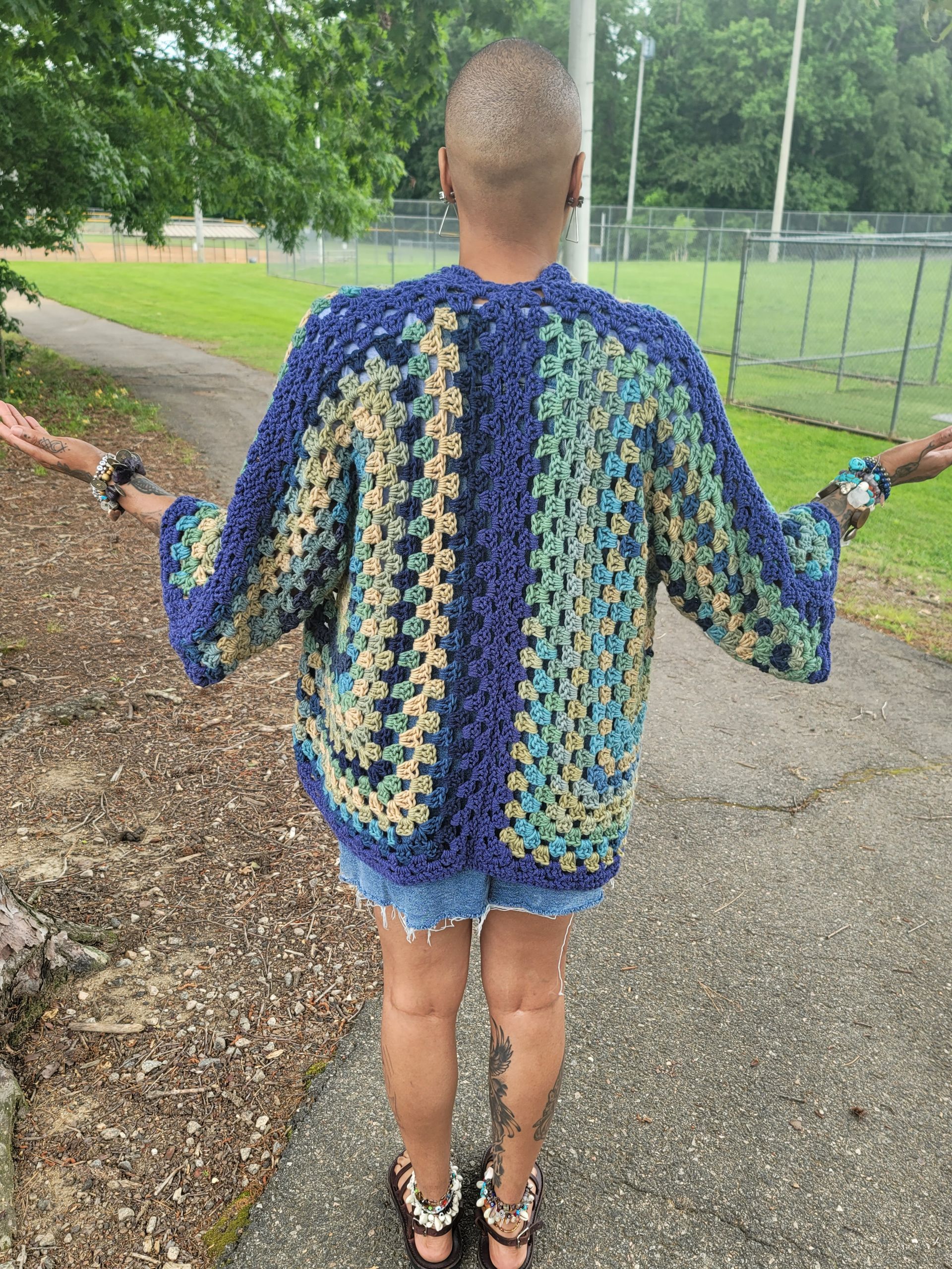 A woman is standing on a sidewalk wearing a crocheted jacket.