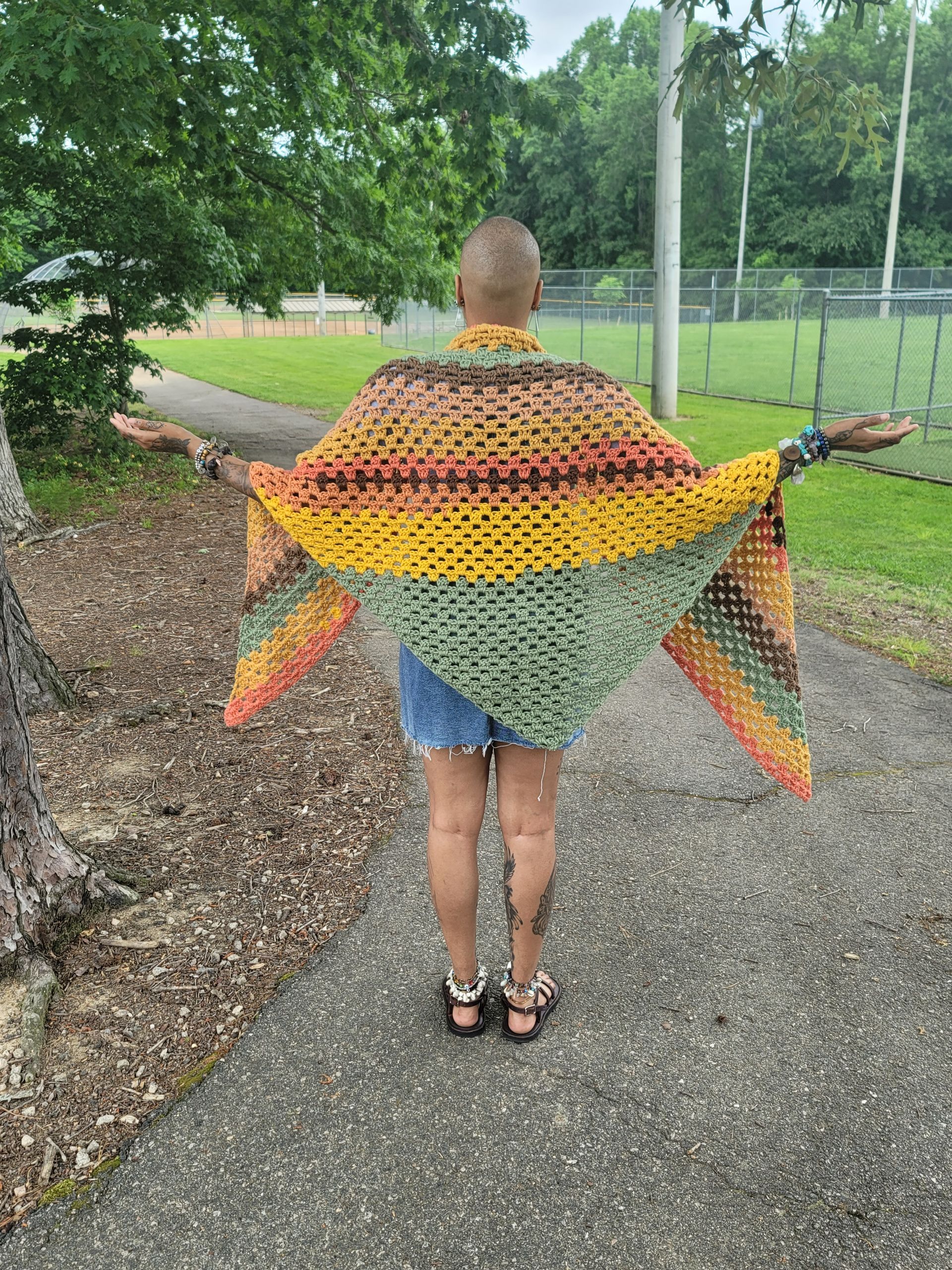 A woman is standing on a sidewalk wearing a crocheted shawl.