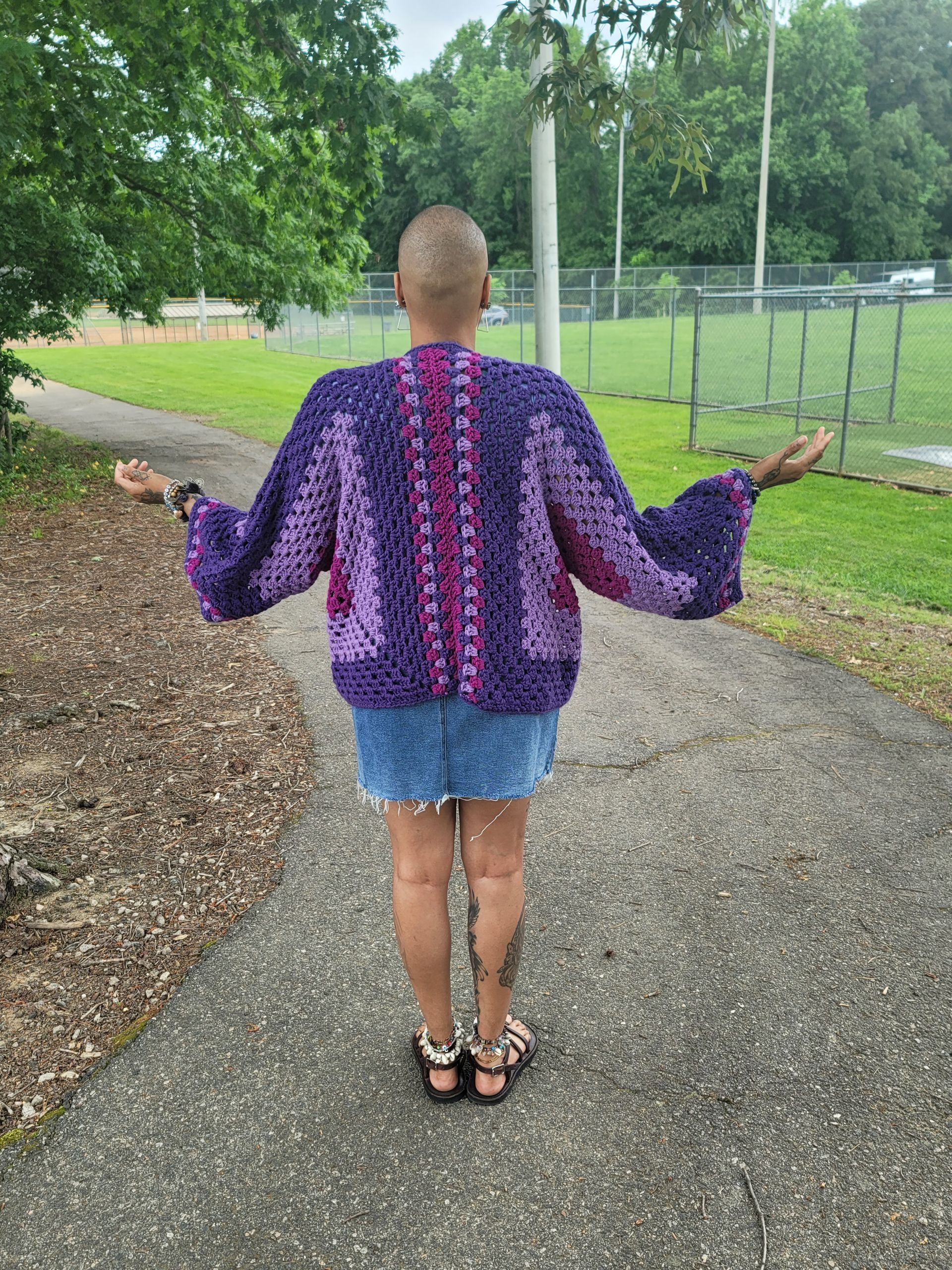 A woman is standing on a sidewalk wearing a purple sweater.