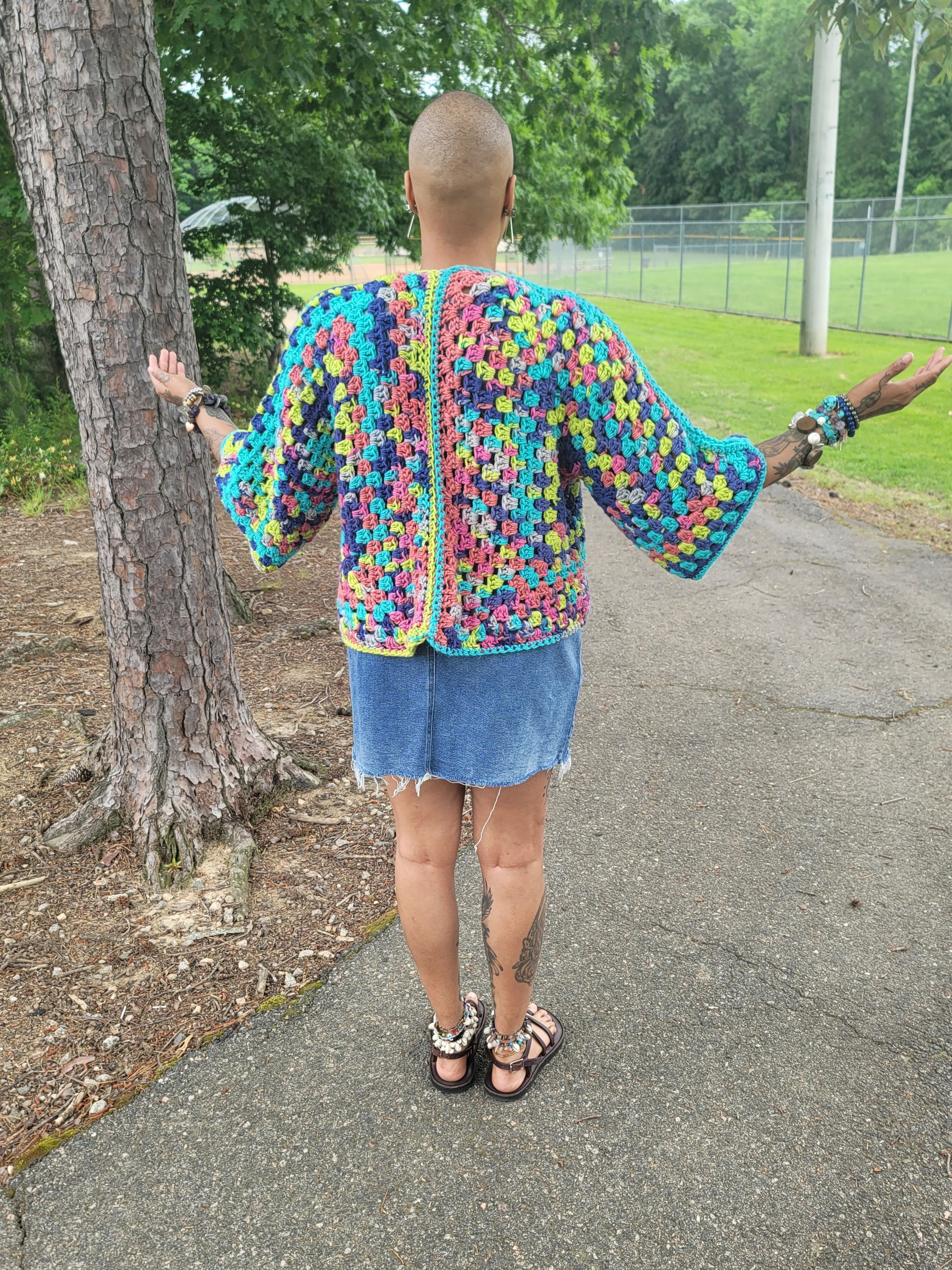 A woman is standing on a sidewalk with her arms outstretched in front of a tree.