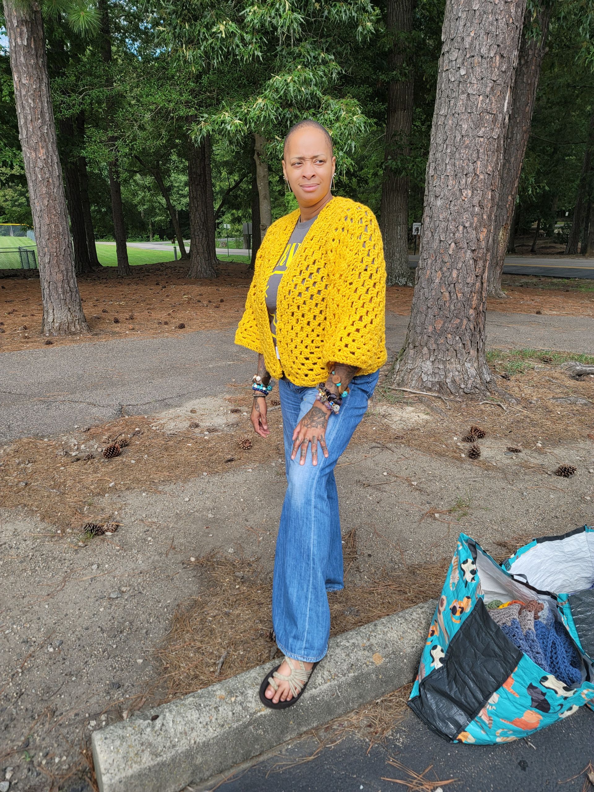 A woman is standing on a curb wearing a yellow crocheted cardigan.