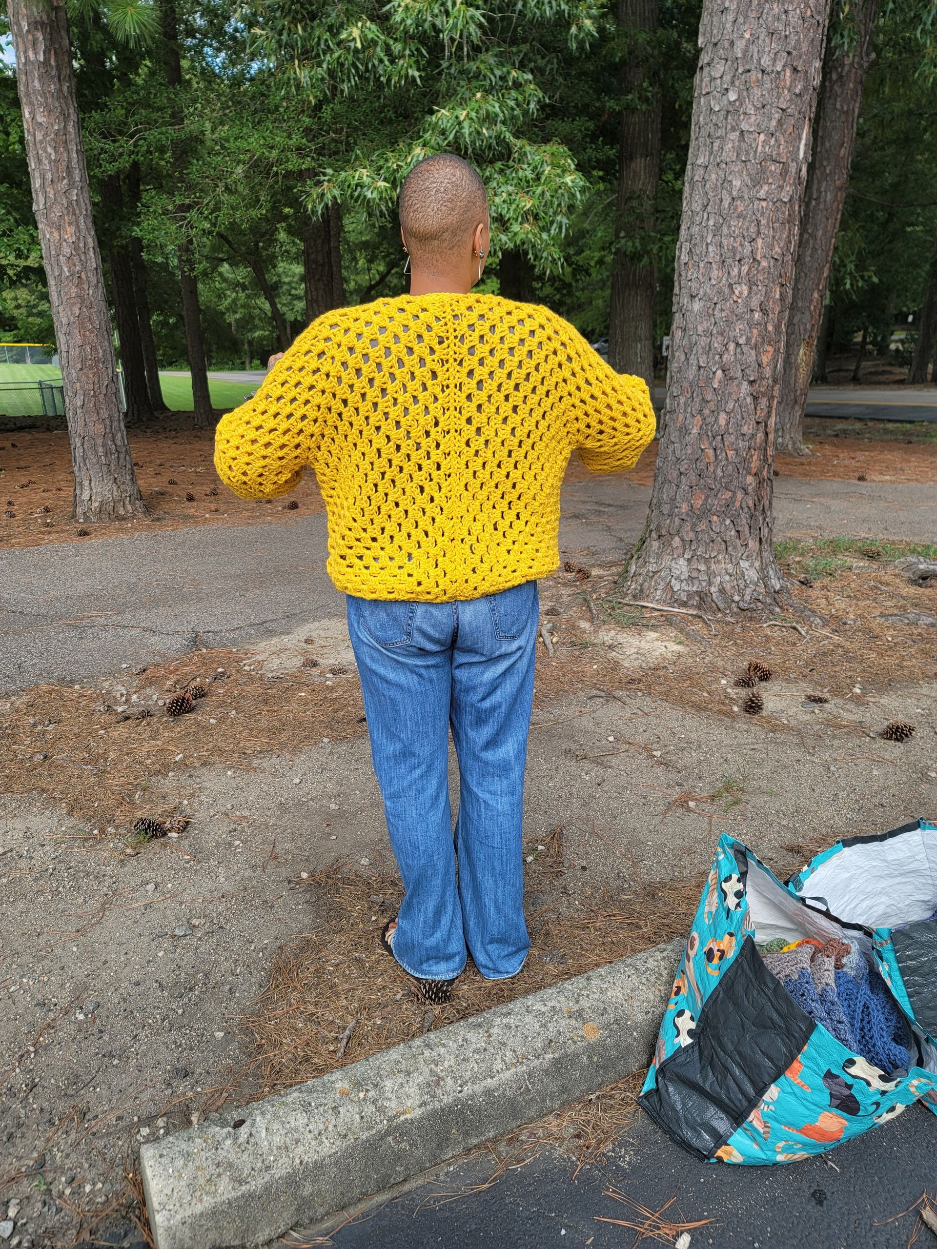 A man wearing a yellow sweater and blue jeans is standing in a parking lot.
