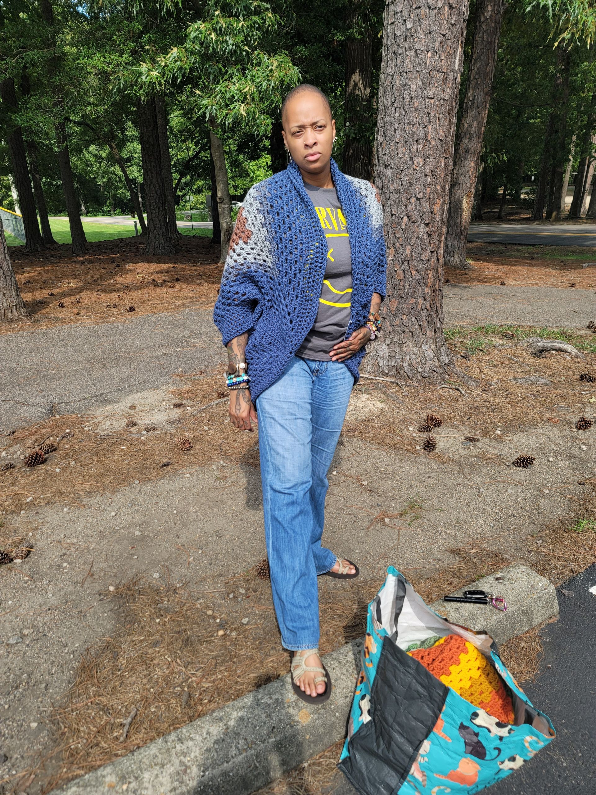 A woman in a blue cardigan and jeans is standing next to a tree.