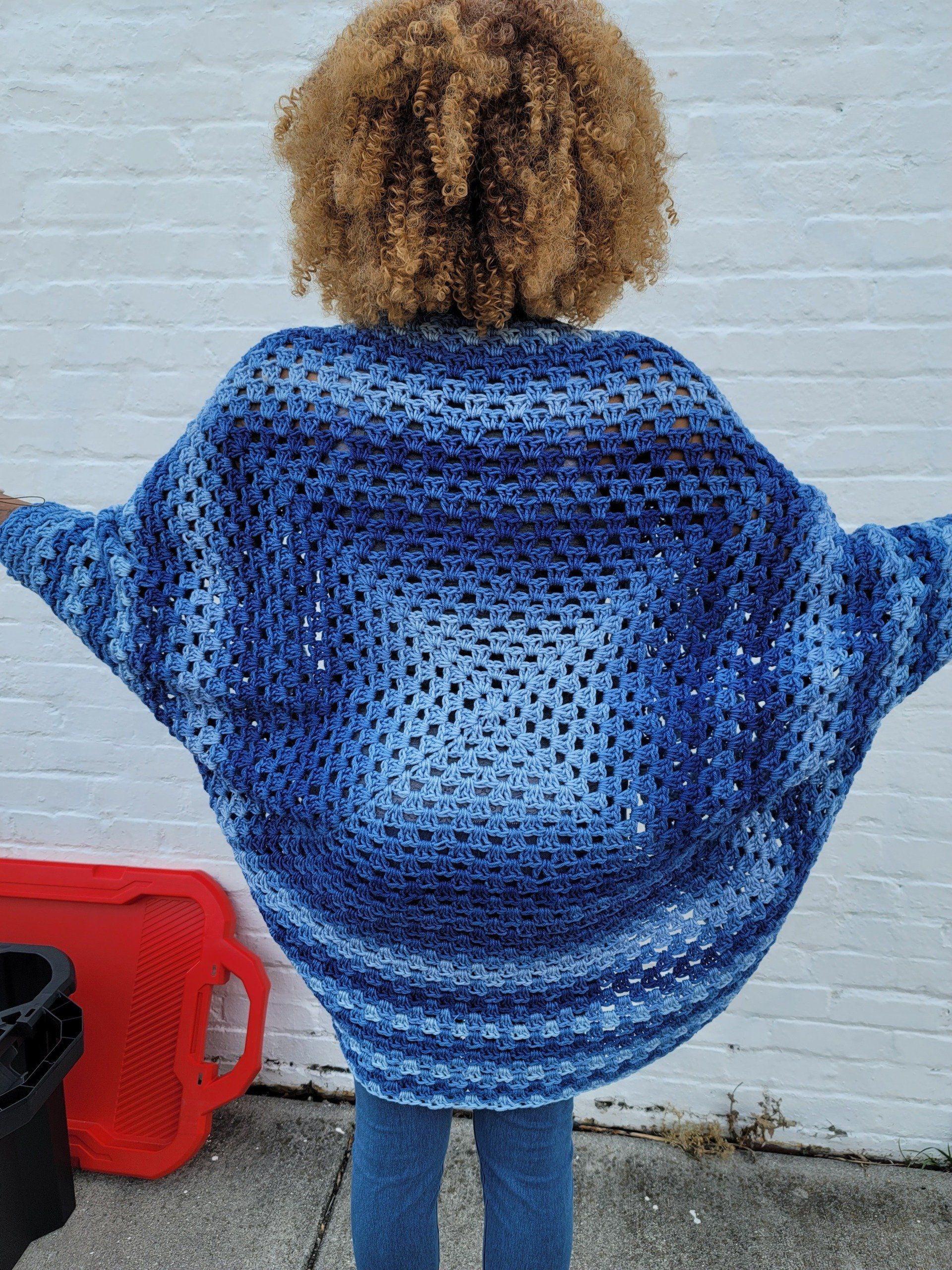 A woman is standing on a sidewalk wearing a blue sweater.