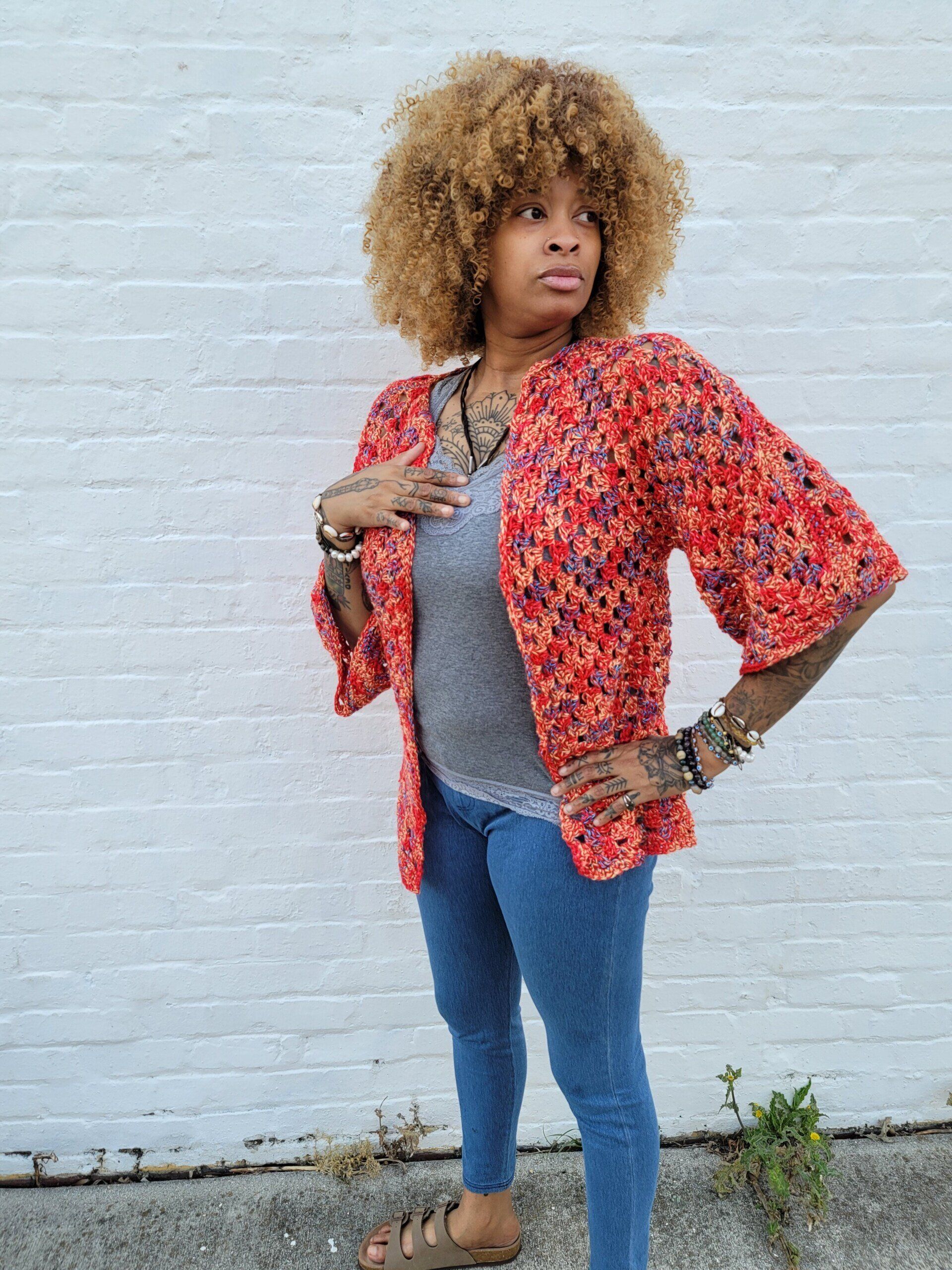A woman wearing a red jacket and jeans is standing in front of a white brick wall.