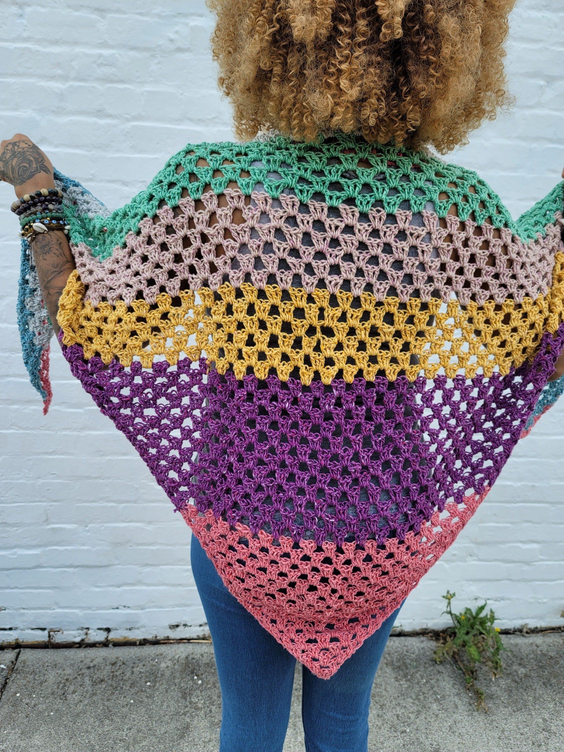 A woman is wearing a colorful crocheted shawl.