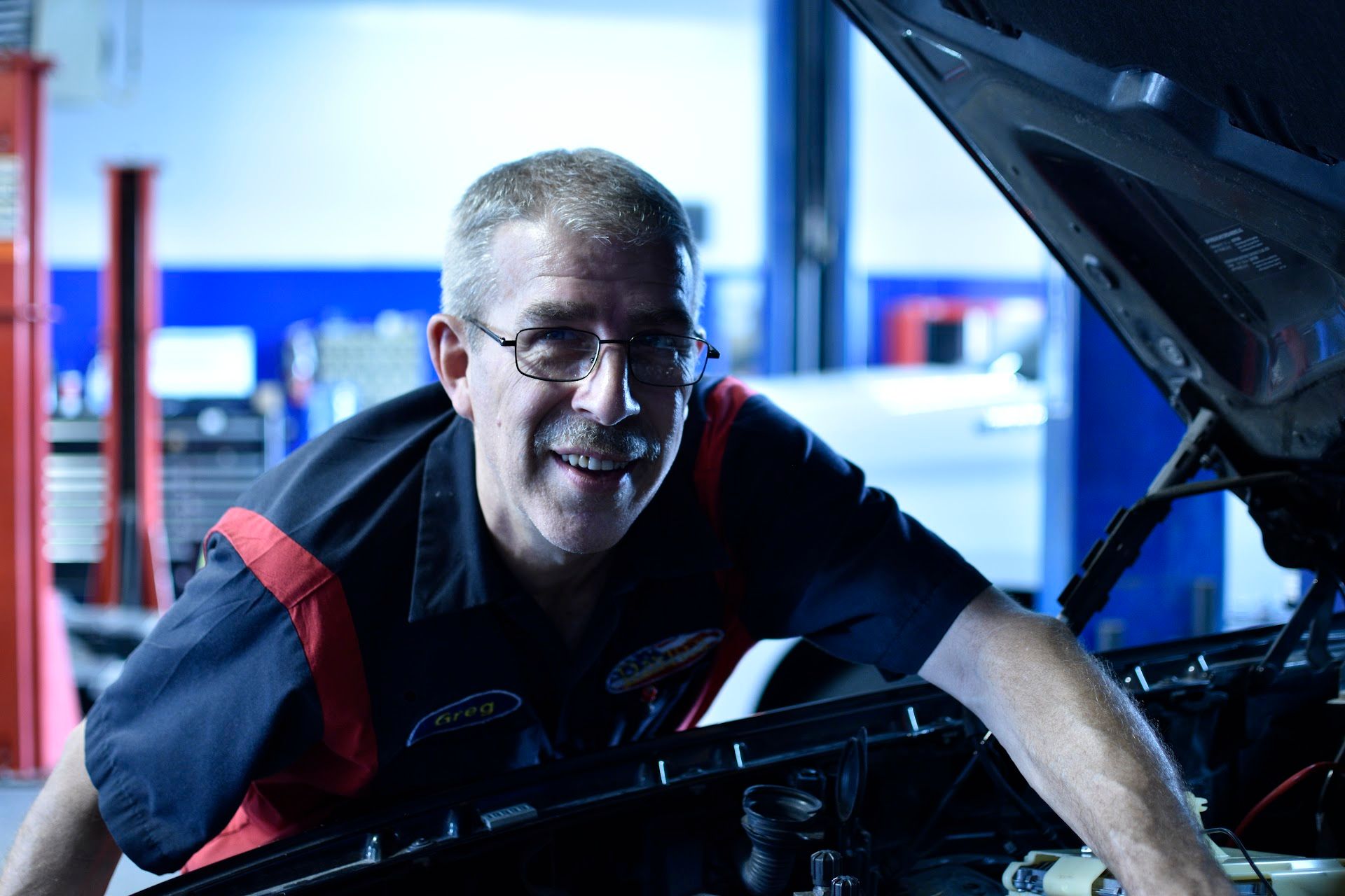 A man is leaning on the hood of a car in a garage | David's Automotive Repair