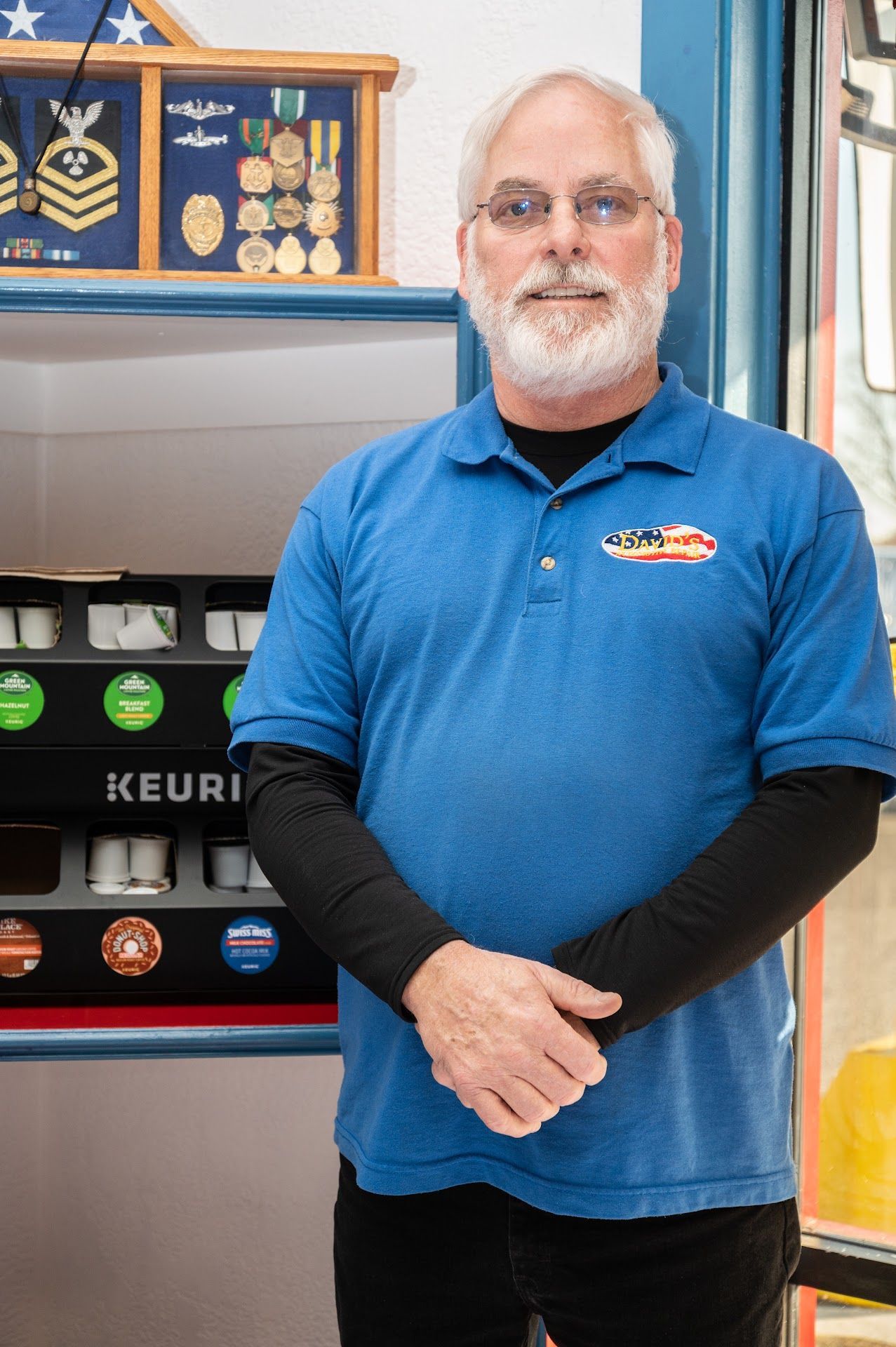 A man in a blue shirt is standing in front of a keurig machine | David's Automotive Repair