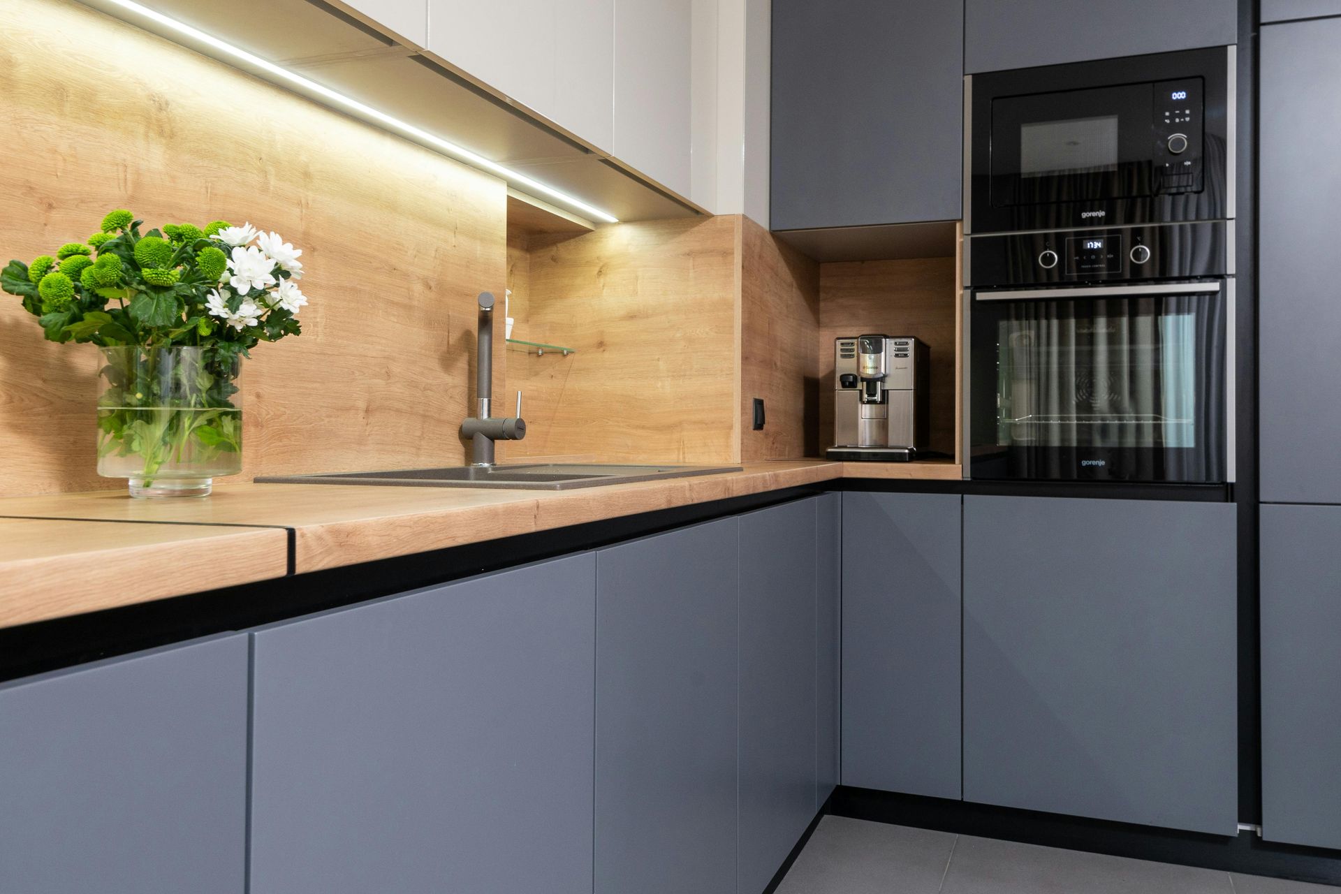 A modern kitchen with gray cabinets , wooden counter tops , a sink , and a microwave oven.