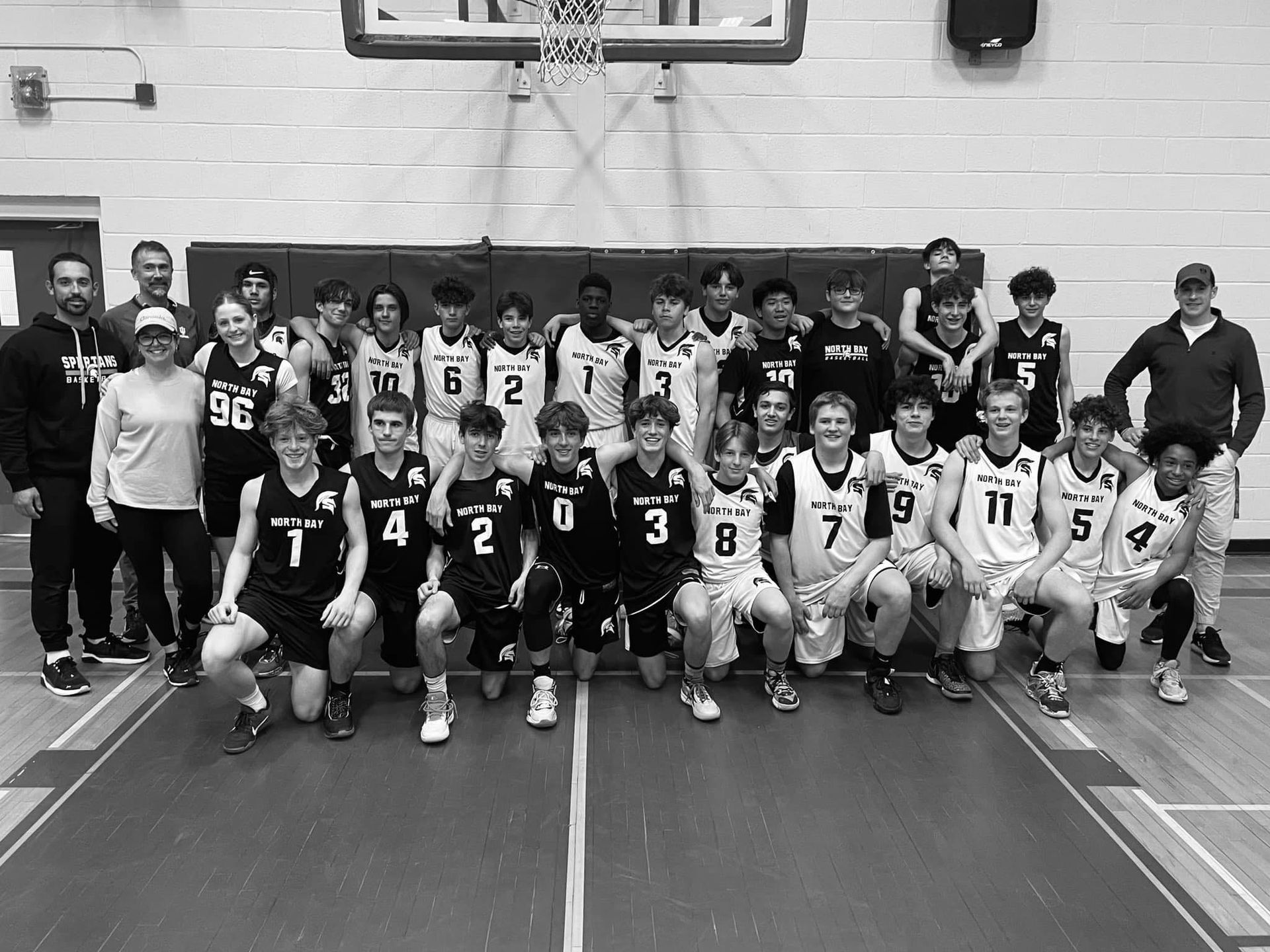 Basketball team photo: Players and coaches pose on court, some kneeling. Black and white photo.