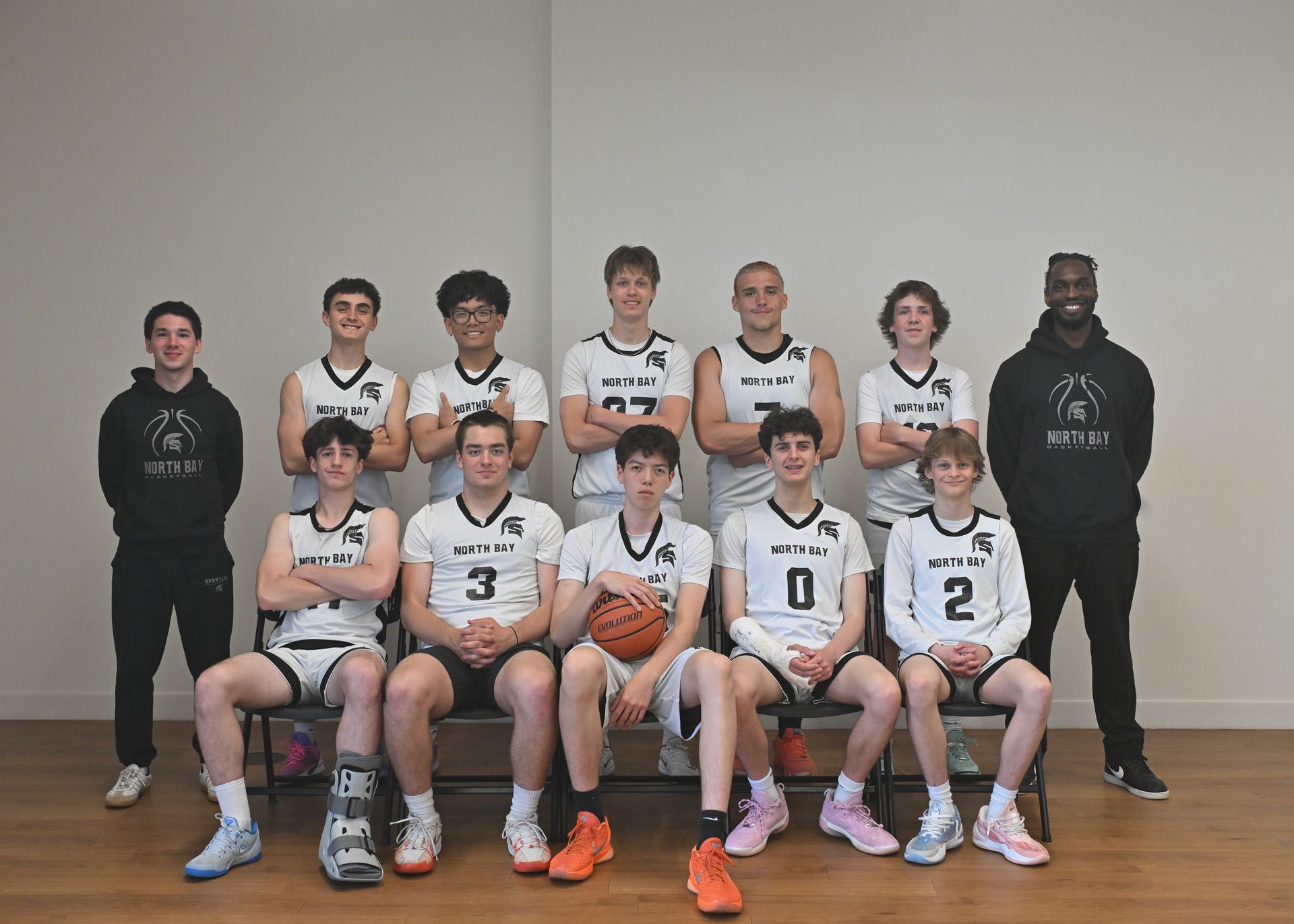 A group of teenage boys and two coaches in black uniforms. Indoor setting, posing.