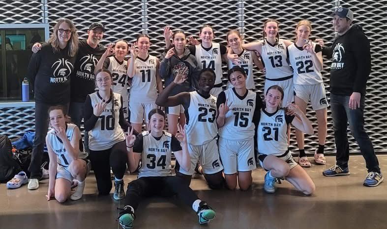 Women's basketball team poses. Black and white uniforms, gesturing, indoors in front of a patterned wall.