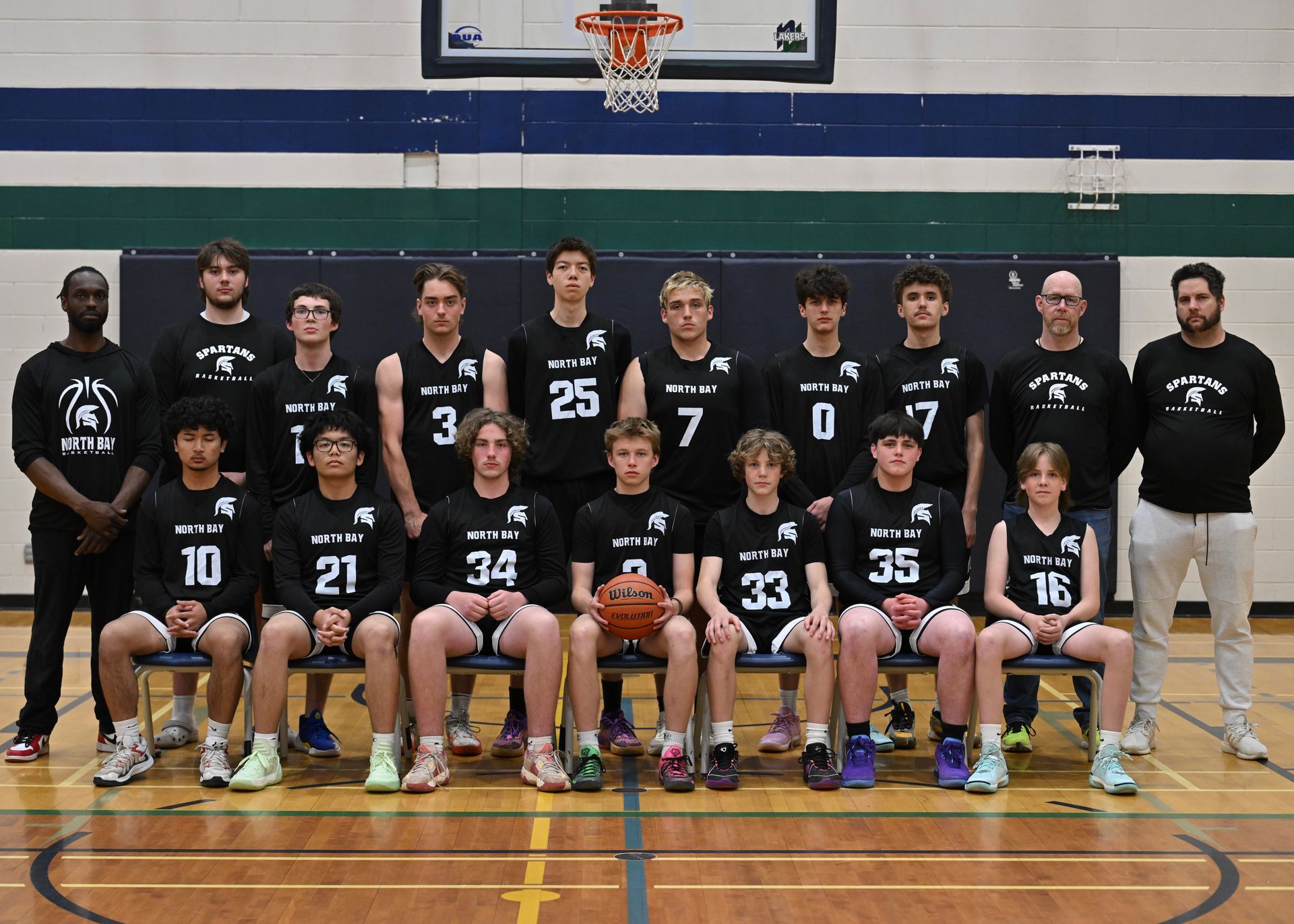 Basketball team photo: group of teenage boys in black jerseys with coaches, posed indoors.