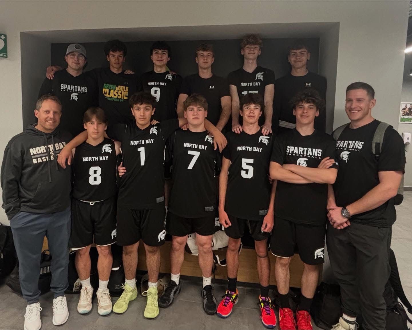 A group of teenage boys and two coaches in black uniforms. Indoor setting, posing.