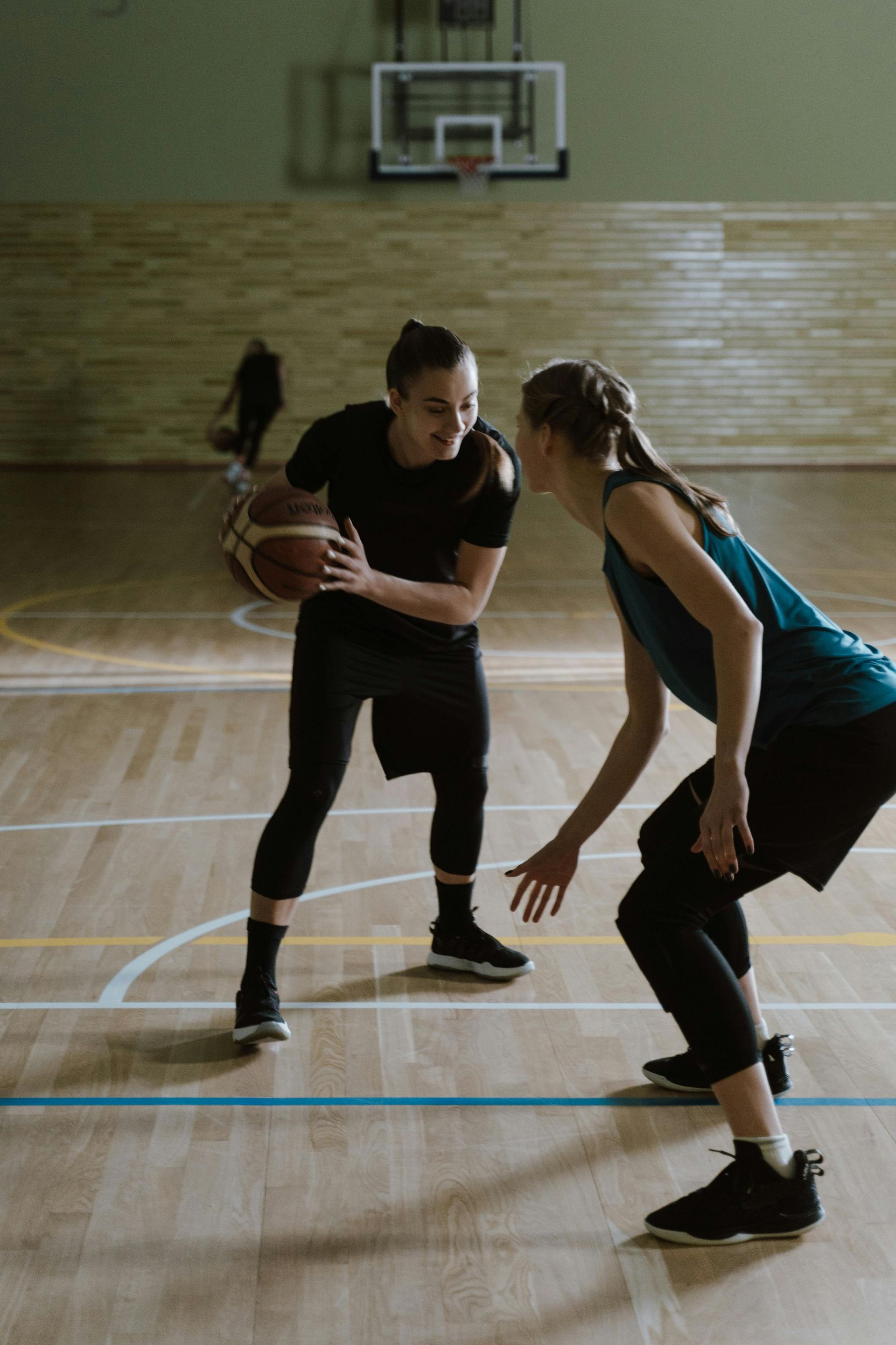 Two women playing basketball on a court. One dribbles, the other defends.