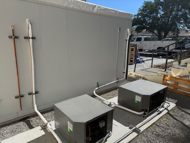 Overhead view of a white commercial refrigeration unit with two fans mounted on a corrugated ceiling.