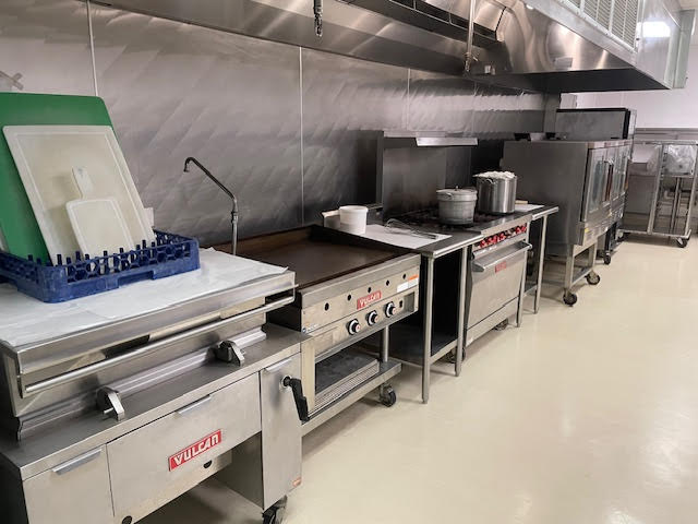 Empty, bright meat processing room with white counters, hooks for hanging meat, and industrial lighting.