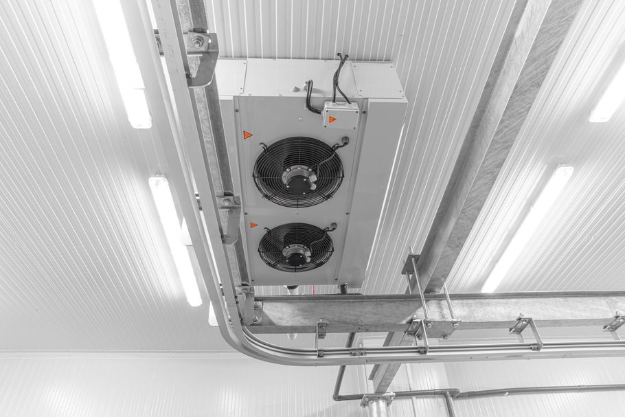 Overhead view of a white commercial refrigeration unit with two fans mounted on a corrugated ceiling.