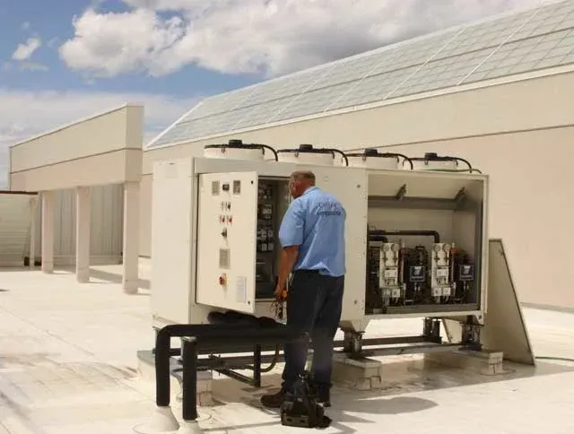 Man in blue shirt working on rooftop air conditioning unit.
