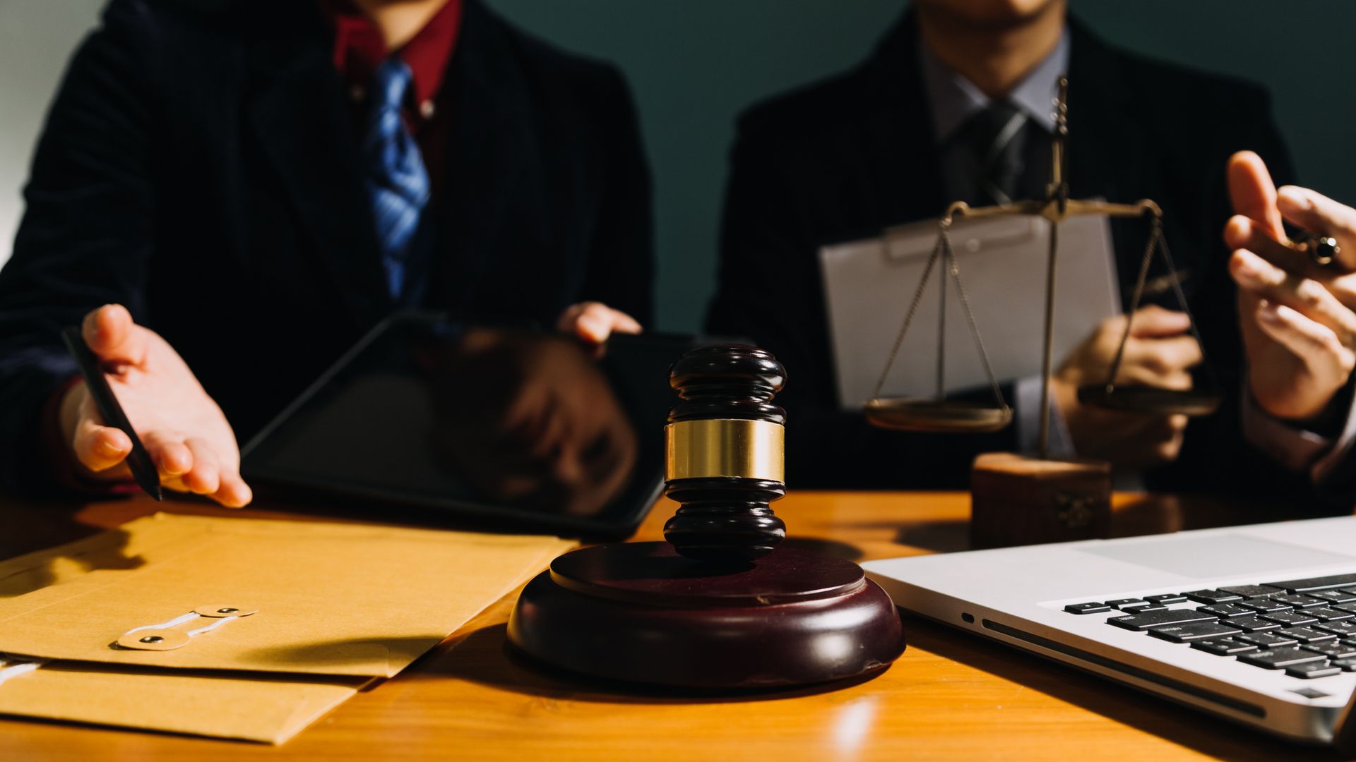 Two lawyers are sitting at a table with a laptop and a judge 's gavel.