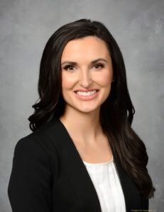 A woman in a black jacket and white shirt is smiling for the camera.