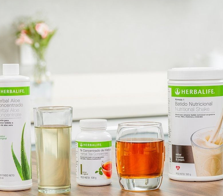 Tres productos nutricionales de Herbalife, que incluyen dos envases y un bote de polvo, junto con dos vasos de líquido.