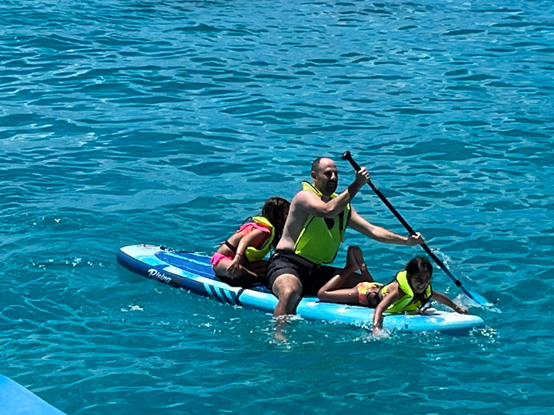 Father sitting on his paddleboard, guiding two children alongside in Mullet Bay
