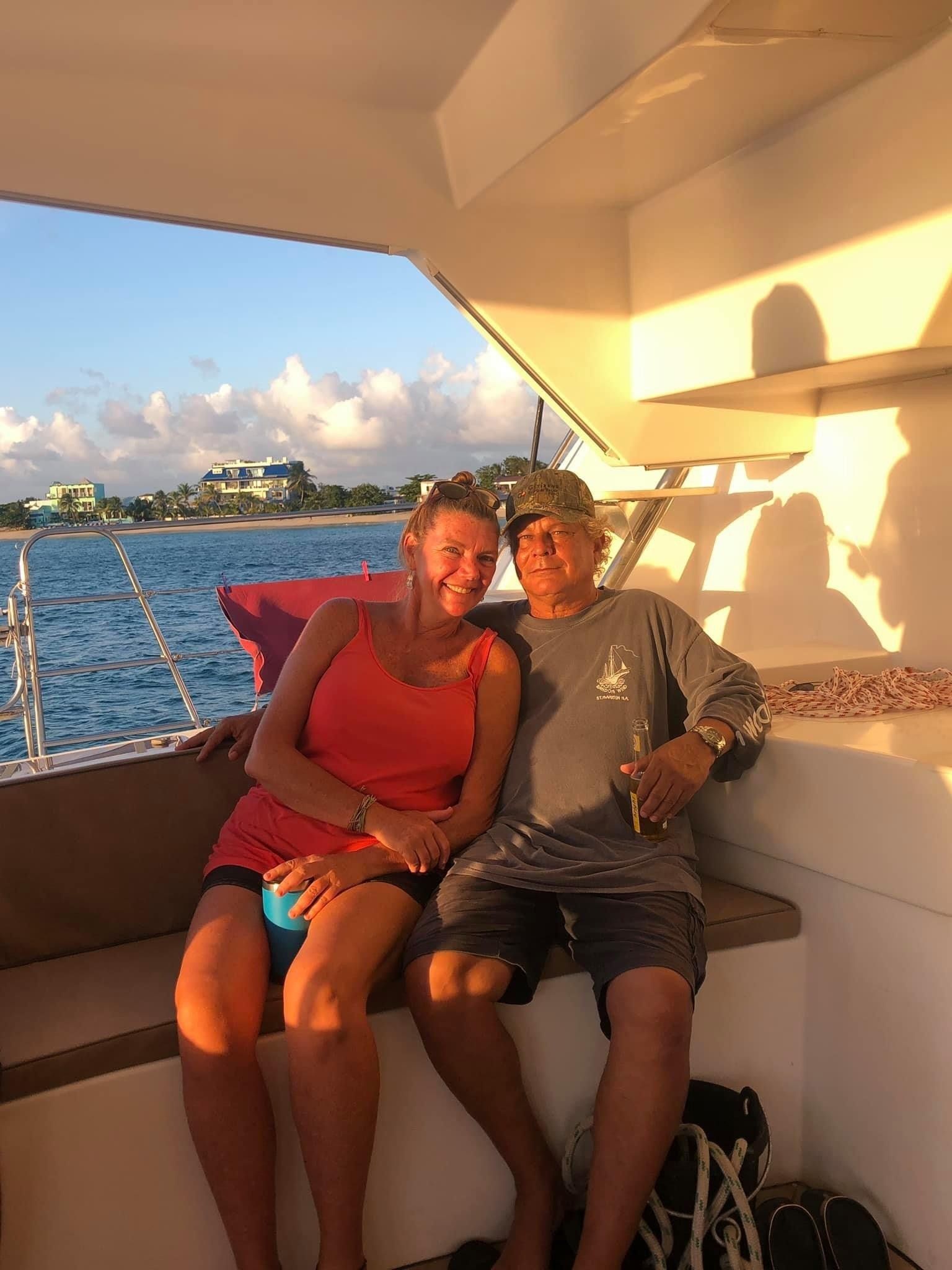 Couple sitting on the aft deck railing of Sail The Phoenix as the sun sets over the horizon