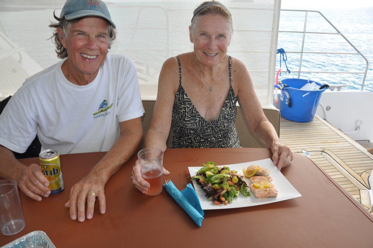Two guests seated at a table aboard Sail The Phoenix, smiling as they sip drinks and enjoy lunch