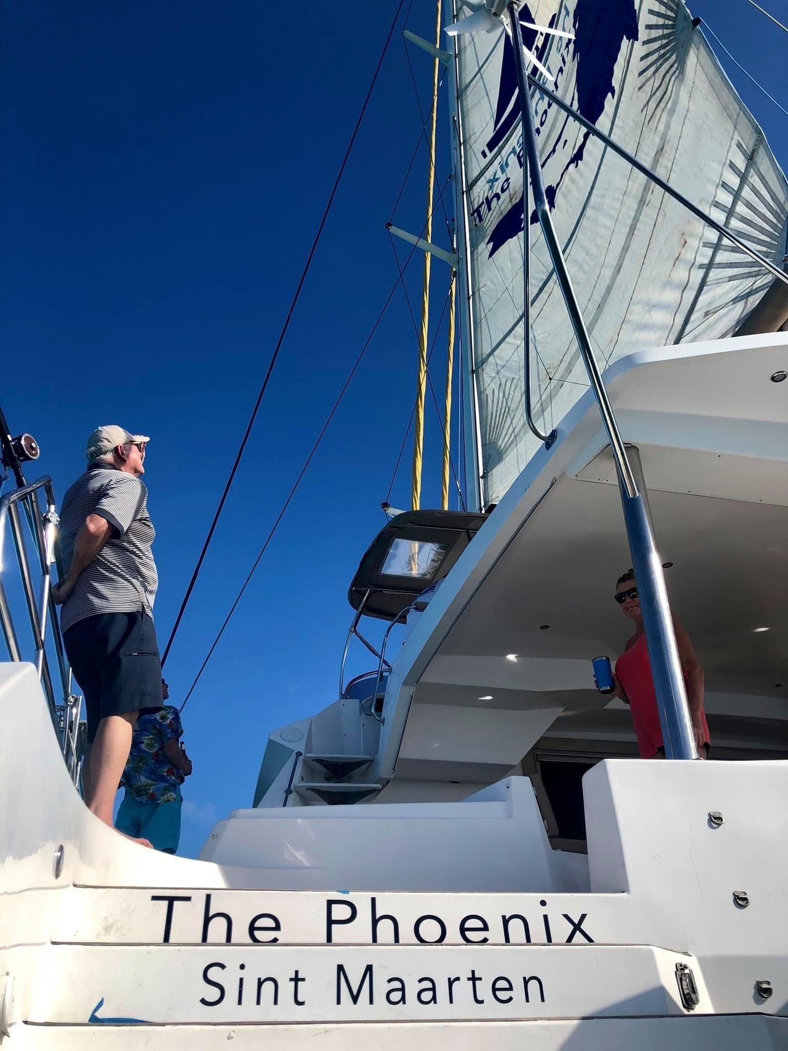 Guest standing on deck of Sail The Phoenix, looking up at its billowing white mainsail