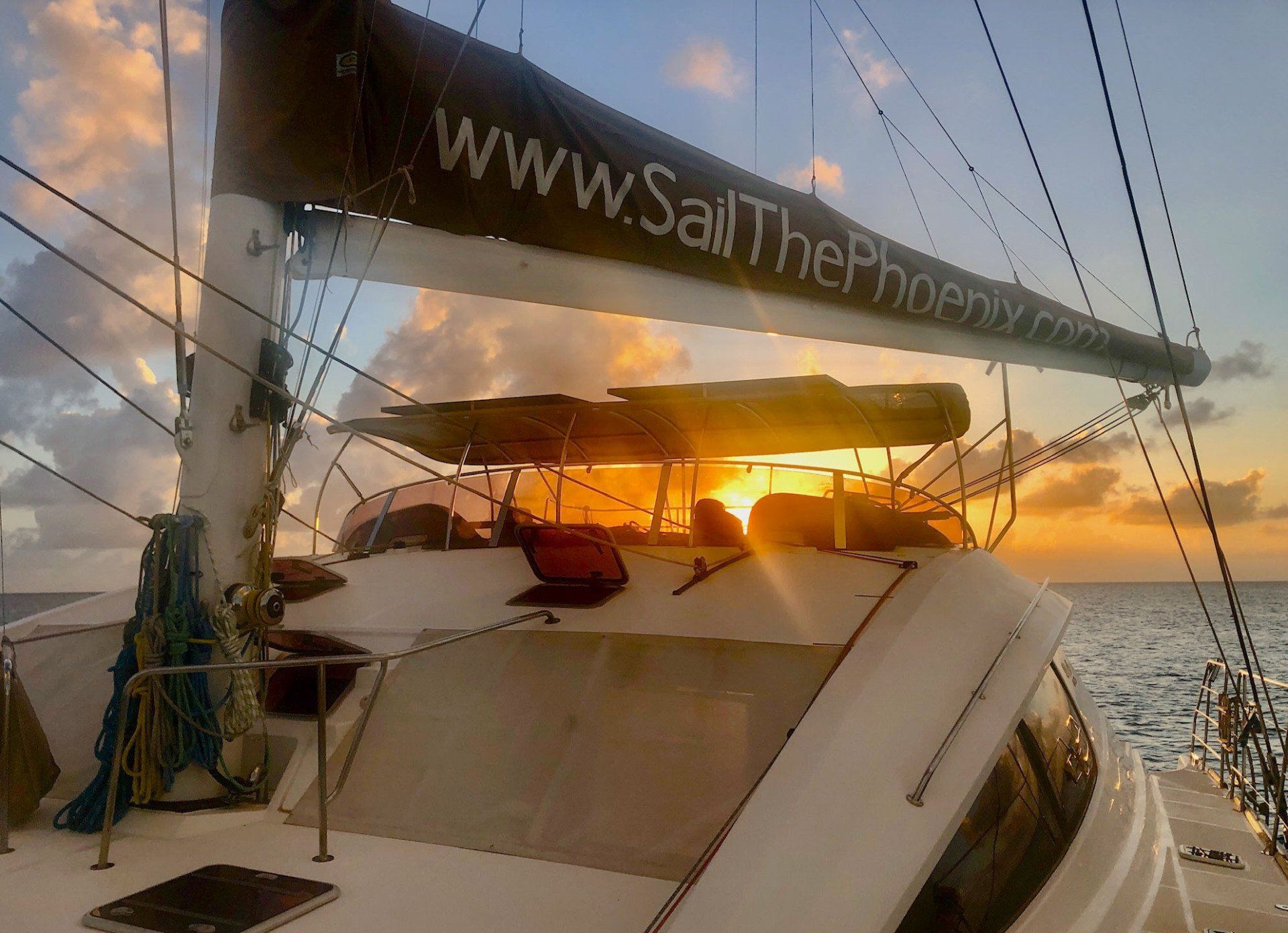 Sailβ―Theβ―Phoenix catamaran silhouetted against a fiery orangeβpink Caribbean sunset