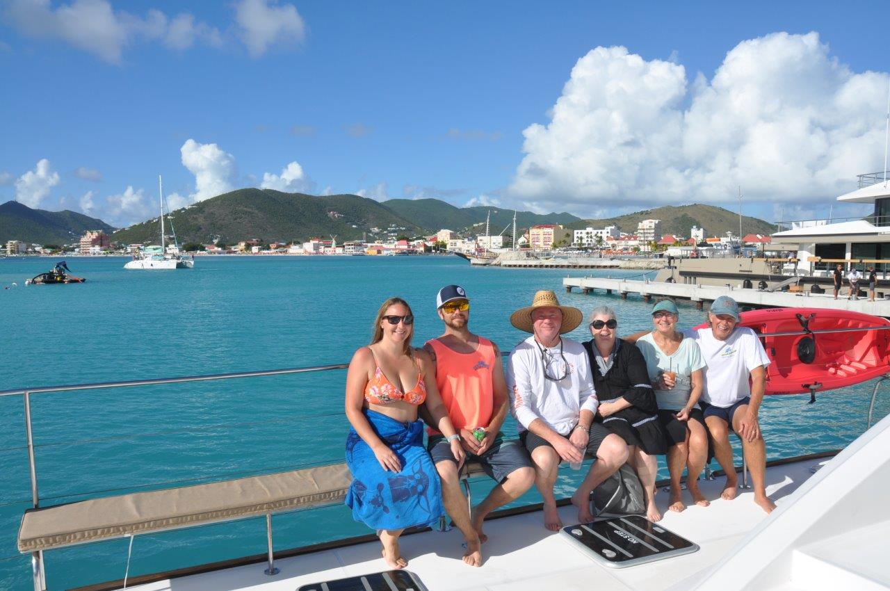 Six guests lounging on the sun bench of Sail The Phoenix with Philipsburg skyline visible across the water