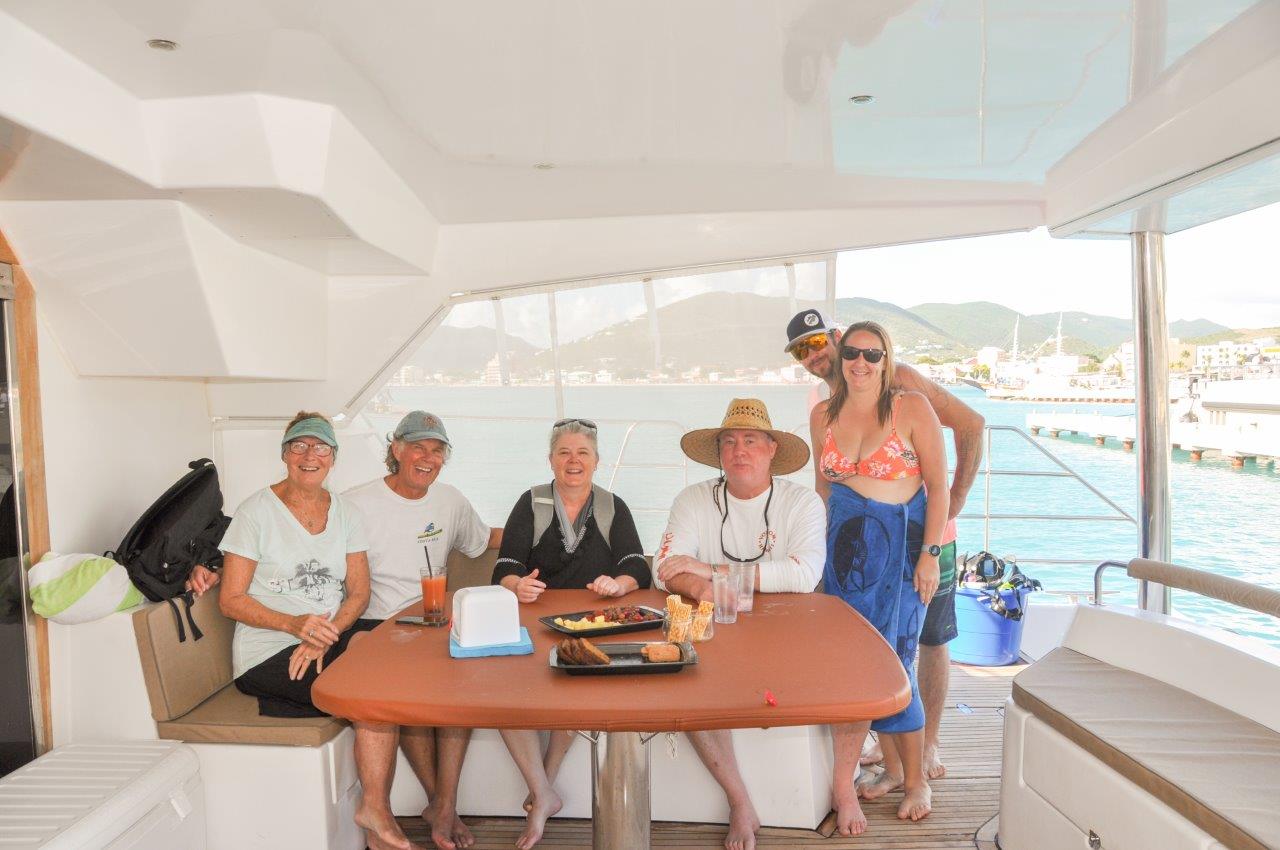 Six guests seated around the aft deck table of Sailβ―Theβ―Phoenix, smiling and enjoying the view