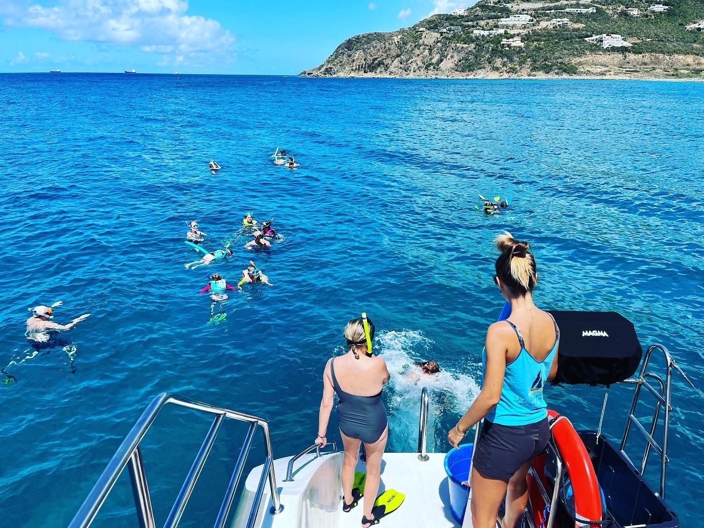 Guests treading water and swimming near Sailβ―Theβ―Phoenix anchored in clear blue seas