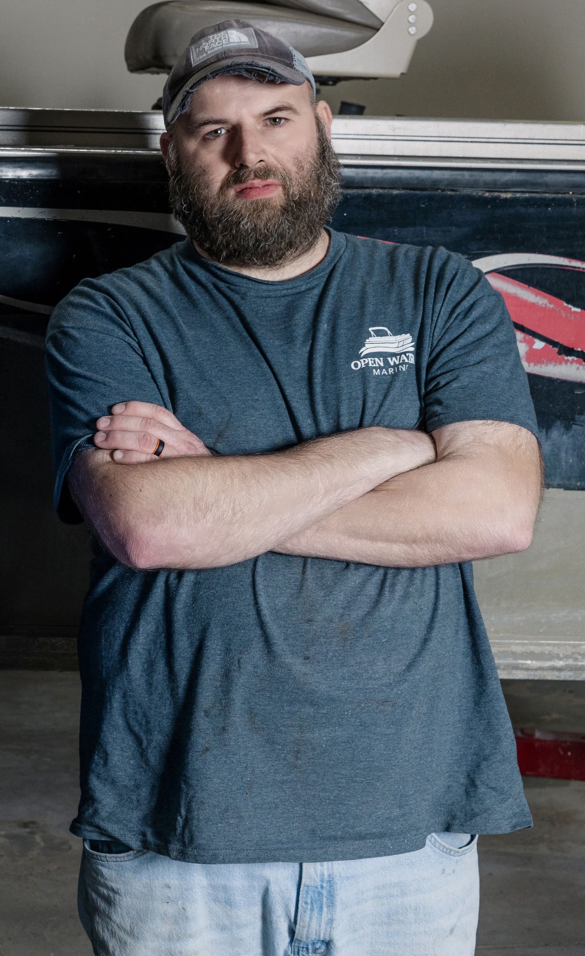 A man with a beard is standing with his arms crossed in front of a boat.