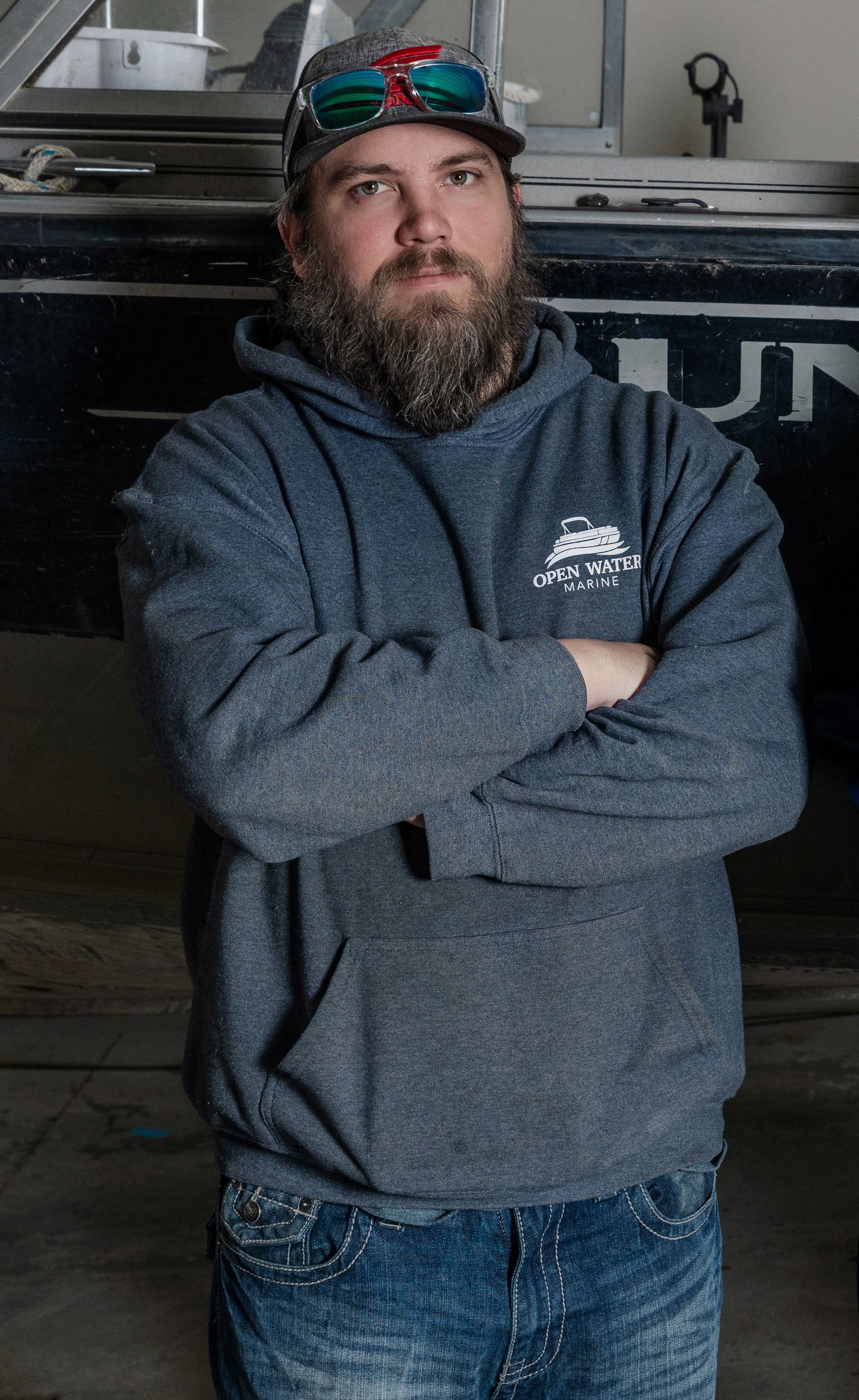A man with a beard is standing with his arms crossed in front of a boat.