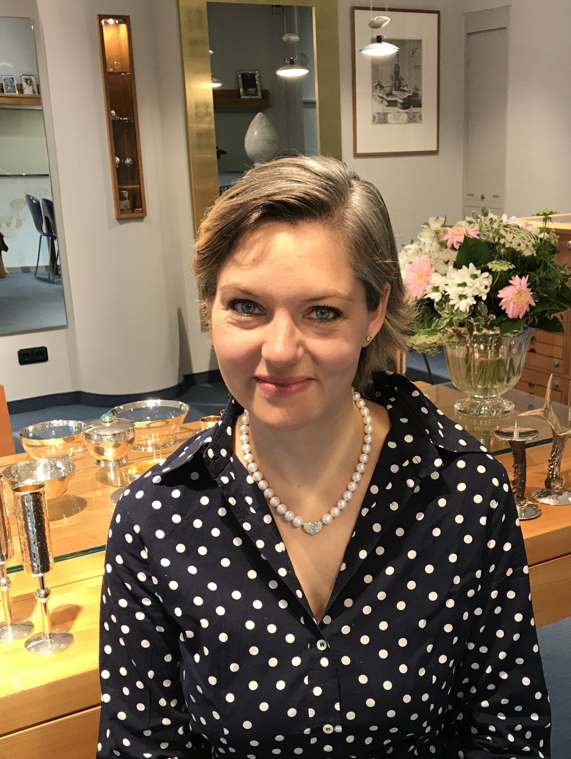 Die Frau trägt ein gepunktetes Hemd und eine Perlenkette.