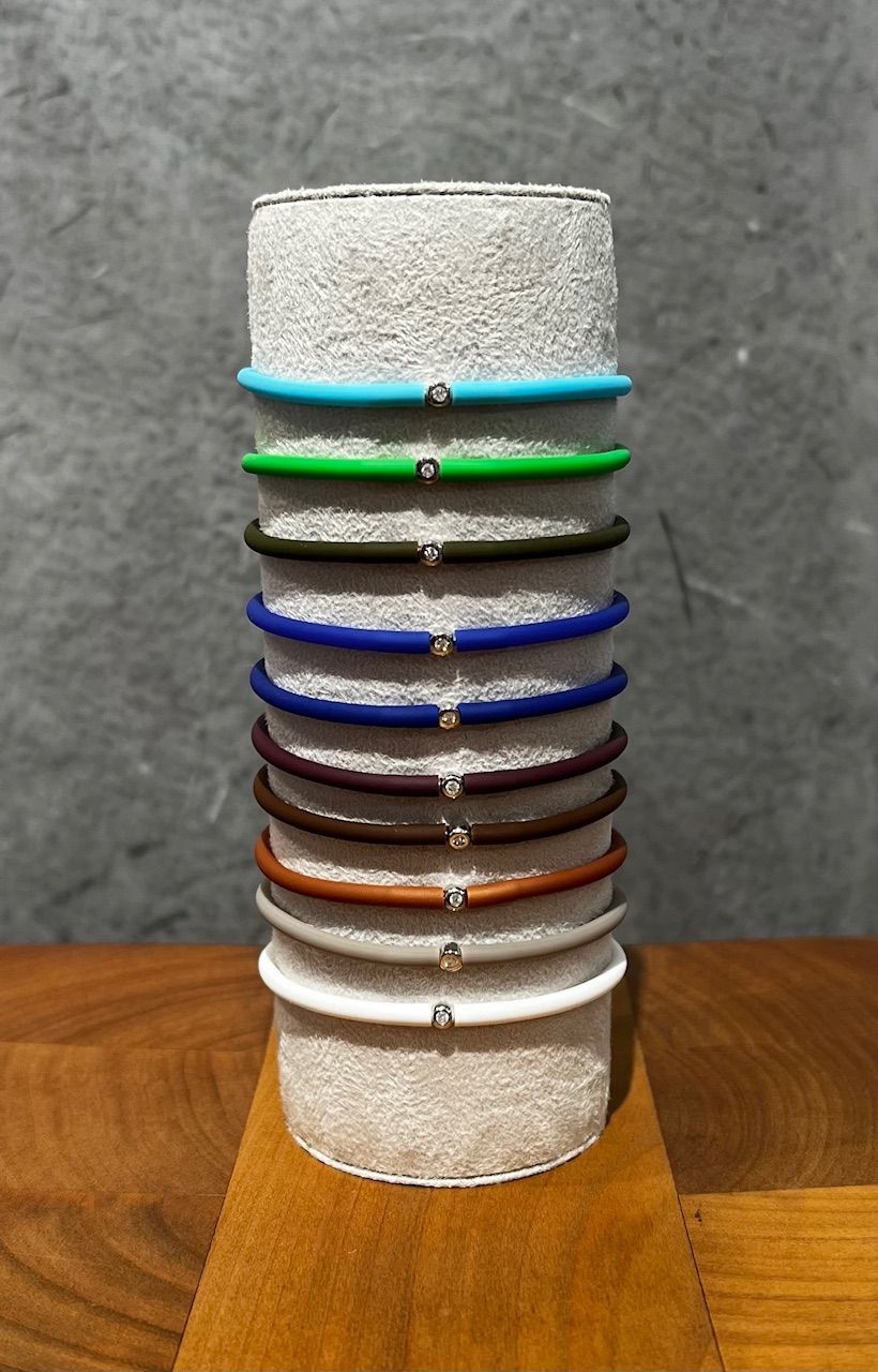 Stapel bunter Armbänder auf einem strukturierten, zylindrischen Ständer, auf einer Holzoberfläche vor grauem Hintergrund.