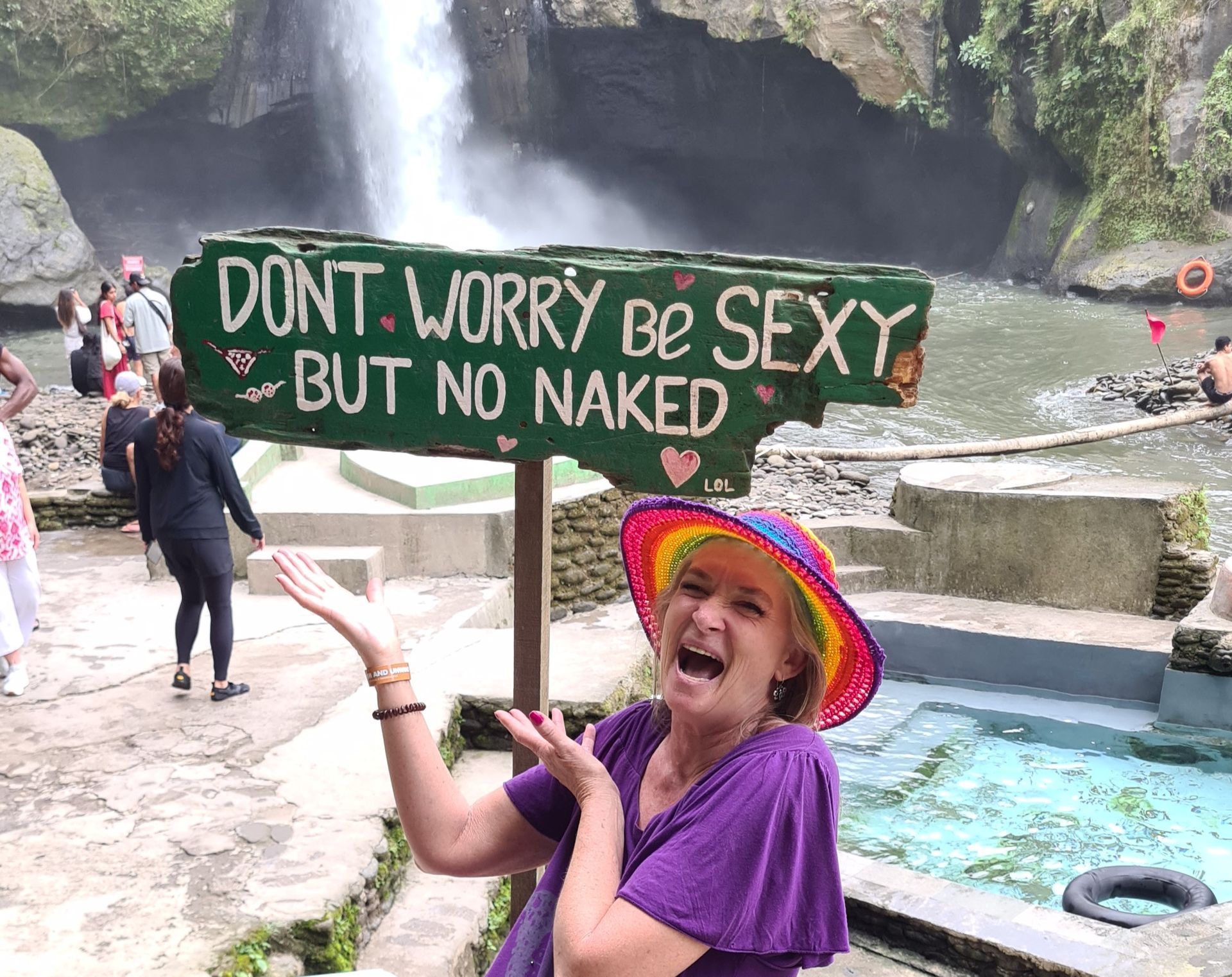 Woman poses excitedly near sign at a waterfall: 
